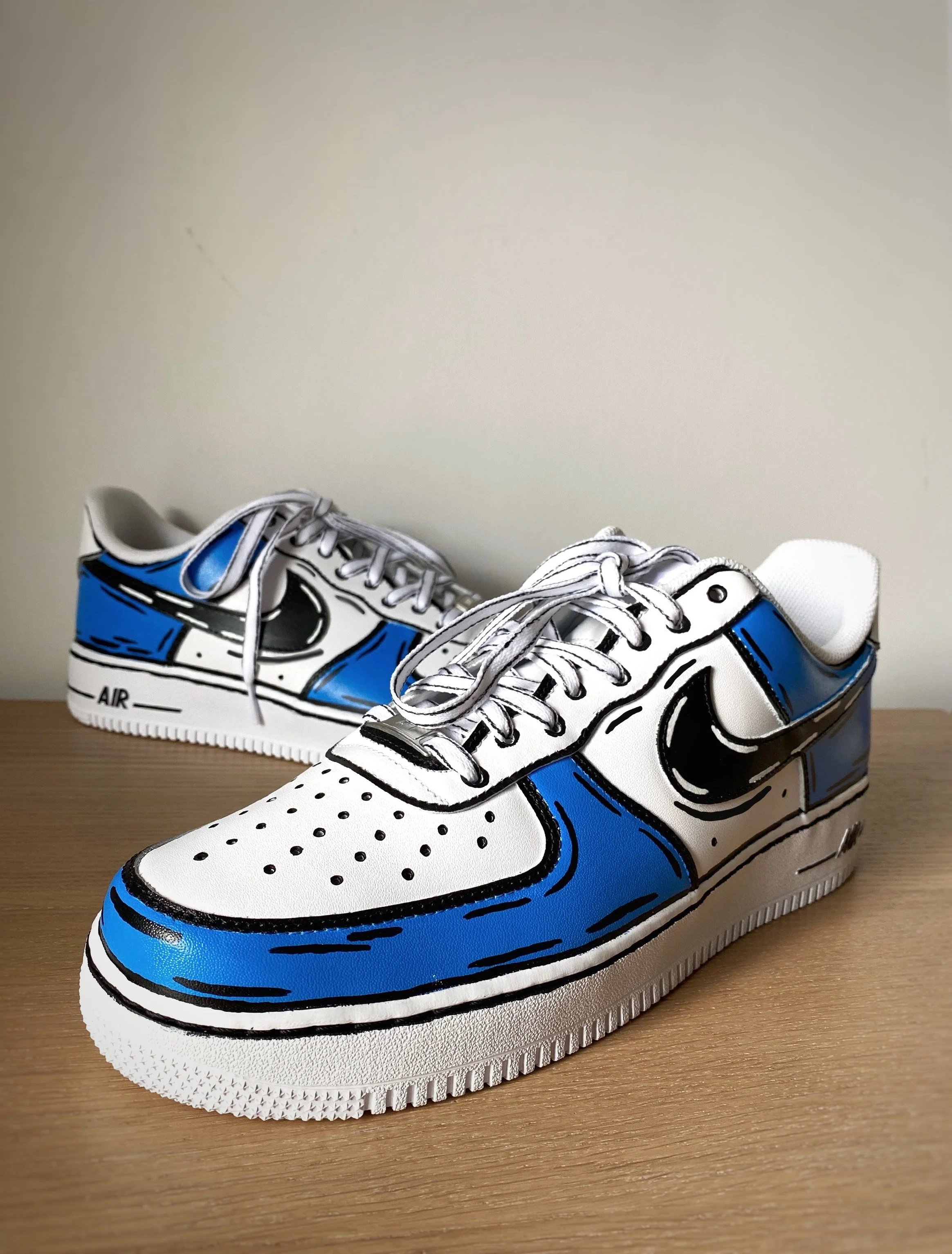 Pair of custom painted Nike sneakers resembling cartoon-style sneakers in white, blue, and black, with hand-drawn details.