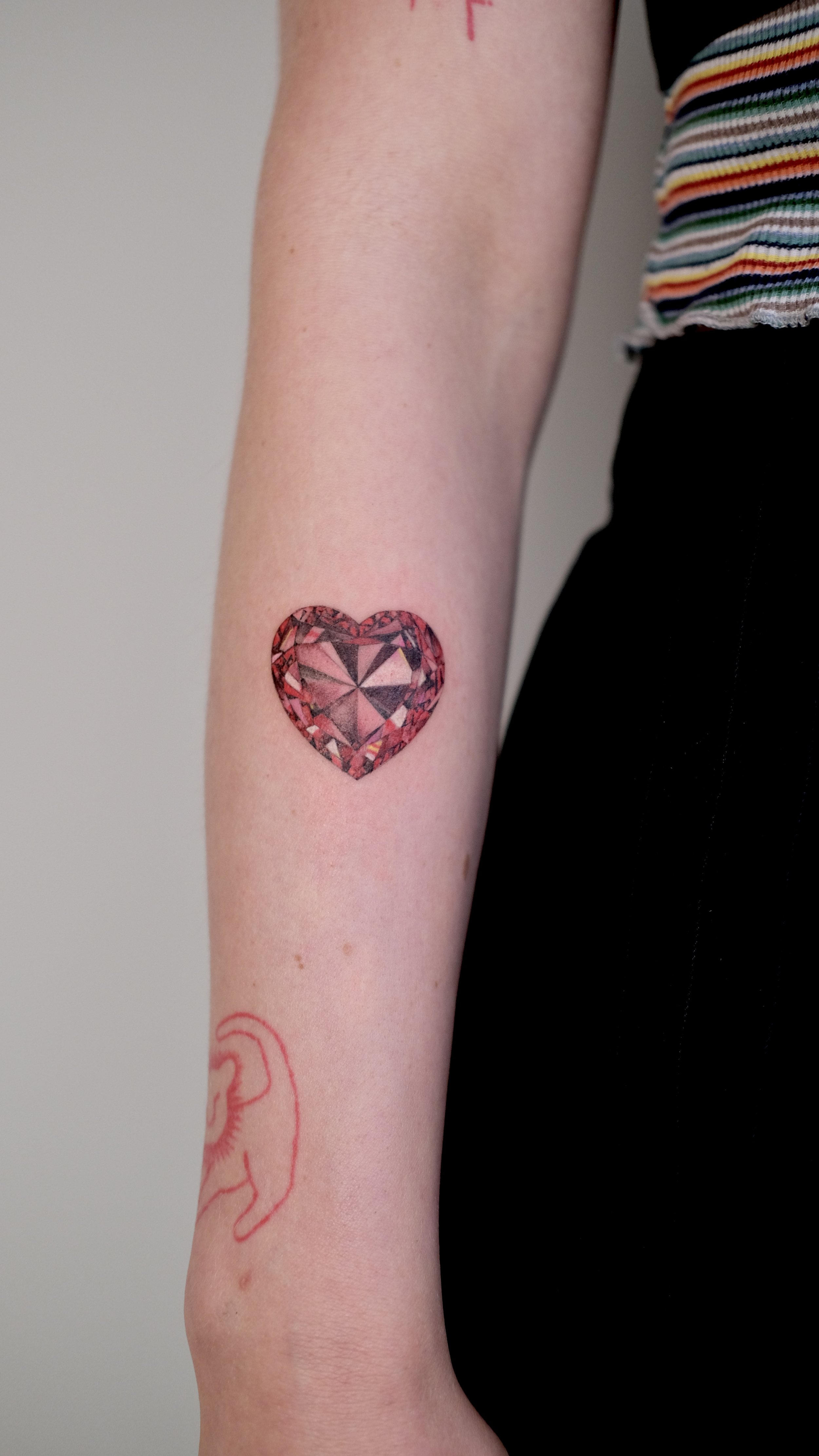 Tattoo of a colorful, geometric heart on person's forearm.