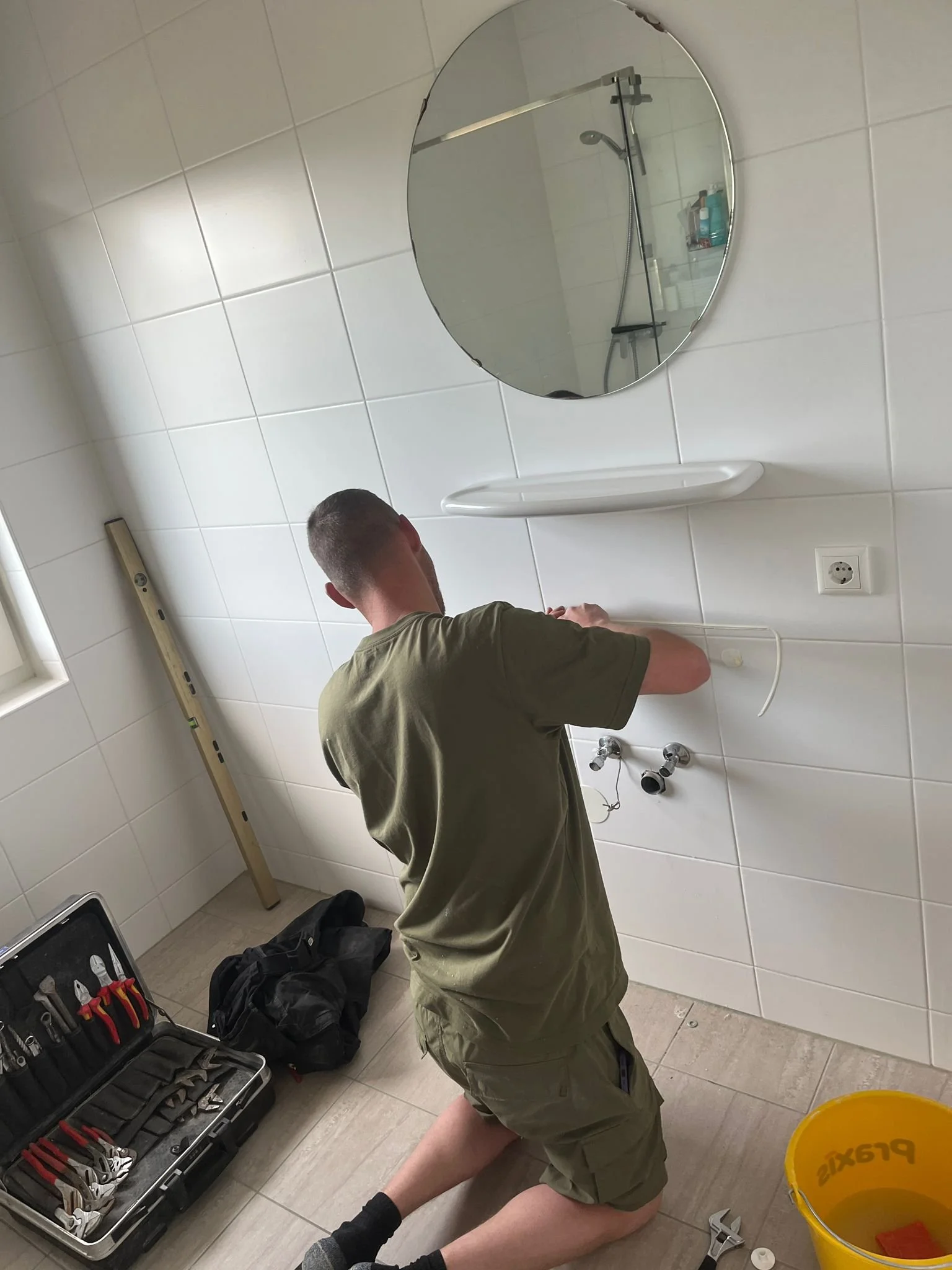 Man werkt in een badkamer, possibly aan de installatie van een wastafel, met gereedschap en een waterpomp.