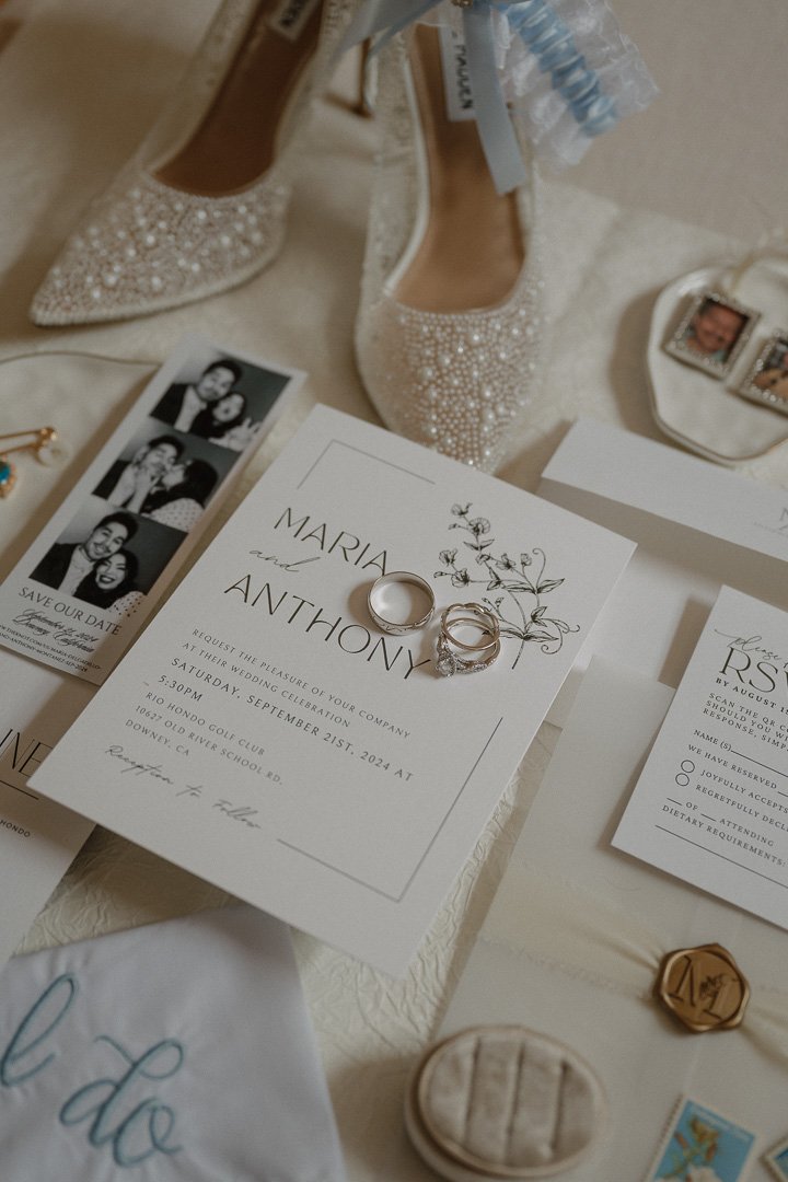 Wedding invitation with rings, a pair of embellished shoes, a photo booth strip, and various wedding details and decor items.