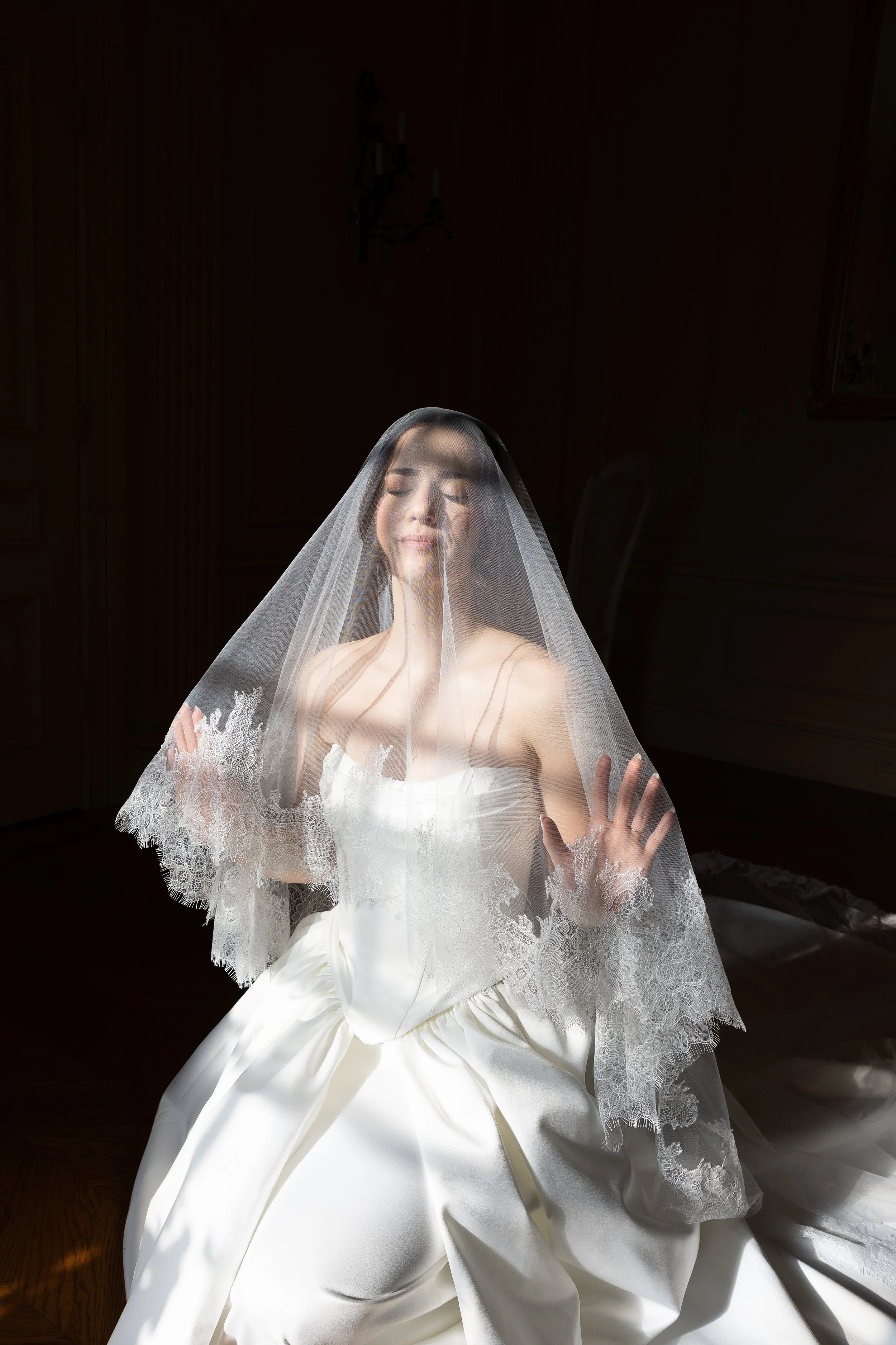 Bride sitting on marble staircase in wedding dress with veil, holding a bouquet of flowers, in an elegant indoor setting.