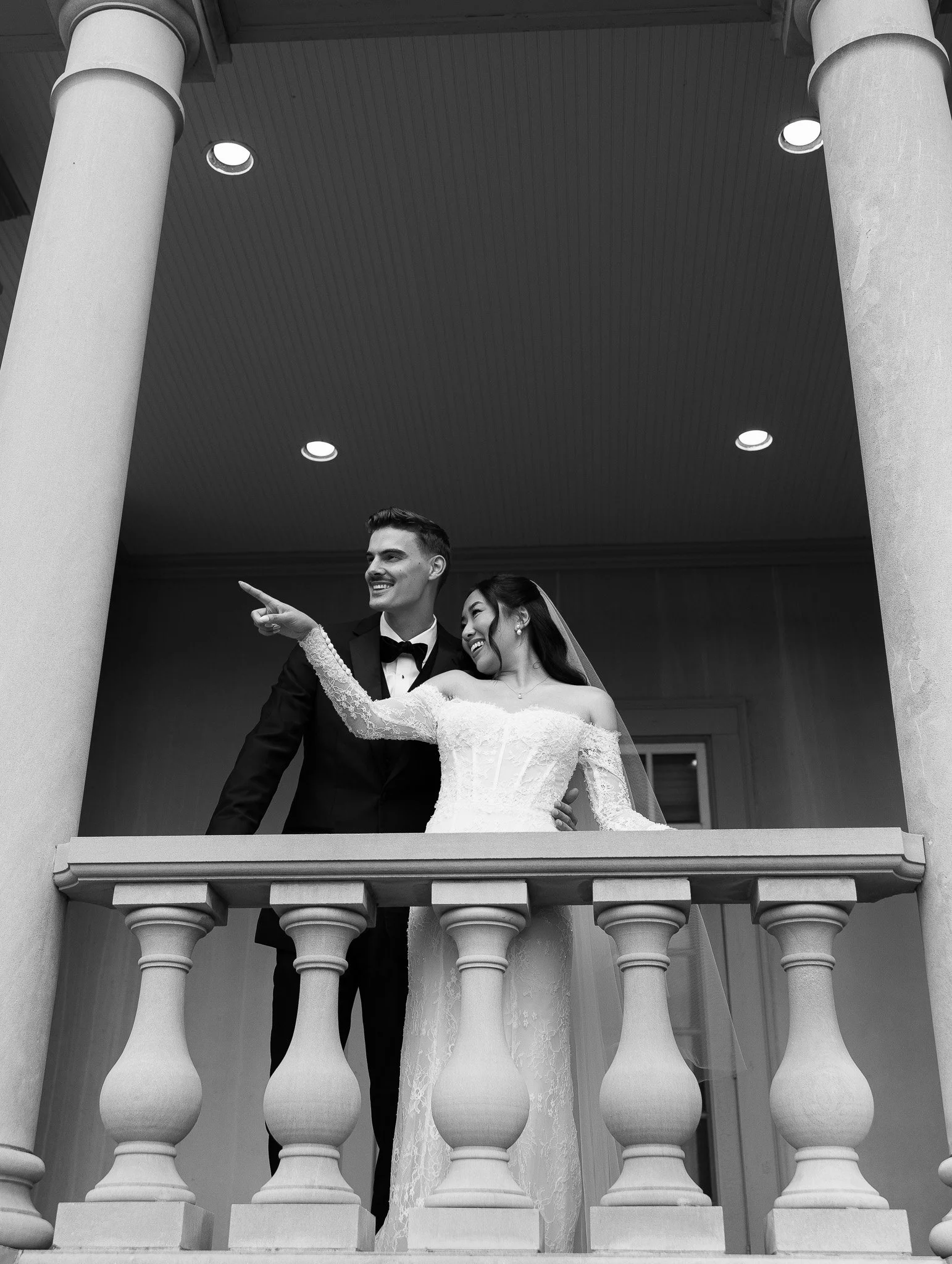 Black and white photo of a newlywed couple sharing a romantic kiss on a crosswalk in an urban street.