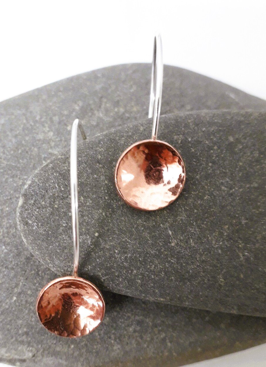 Silver and copper earrings with a hammered round copper disc, resting on a black stone with a white background.