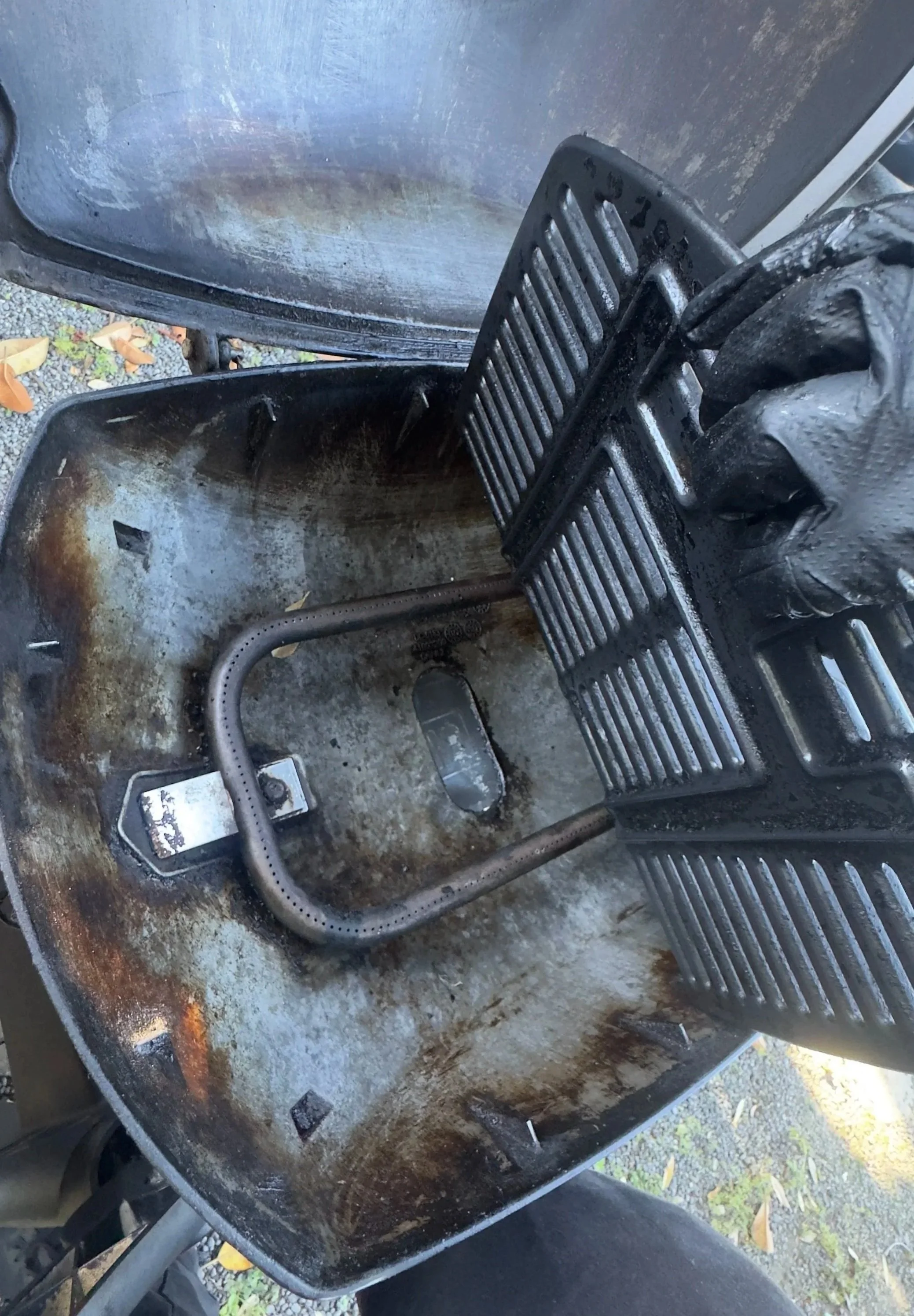 Inside of a rusty and dirty metal barbecue grill with the cooking grate removed, showing the burned interior.