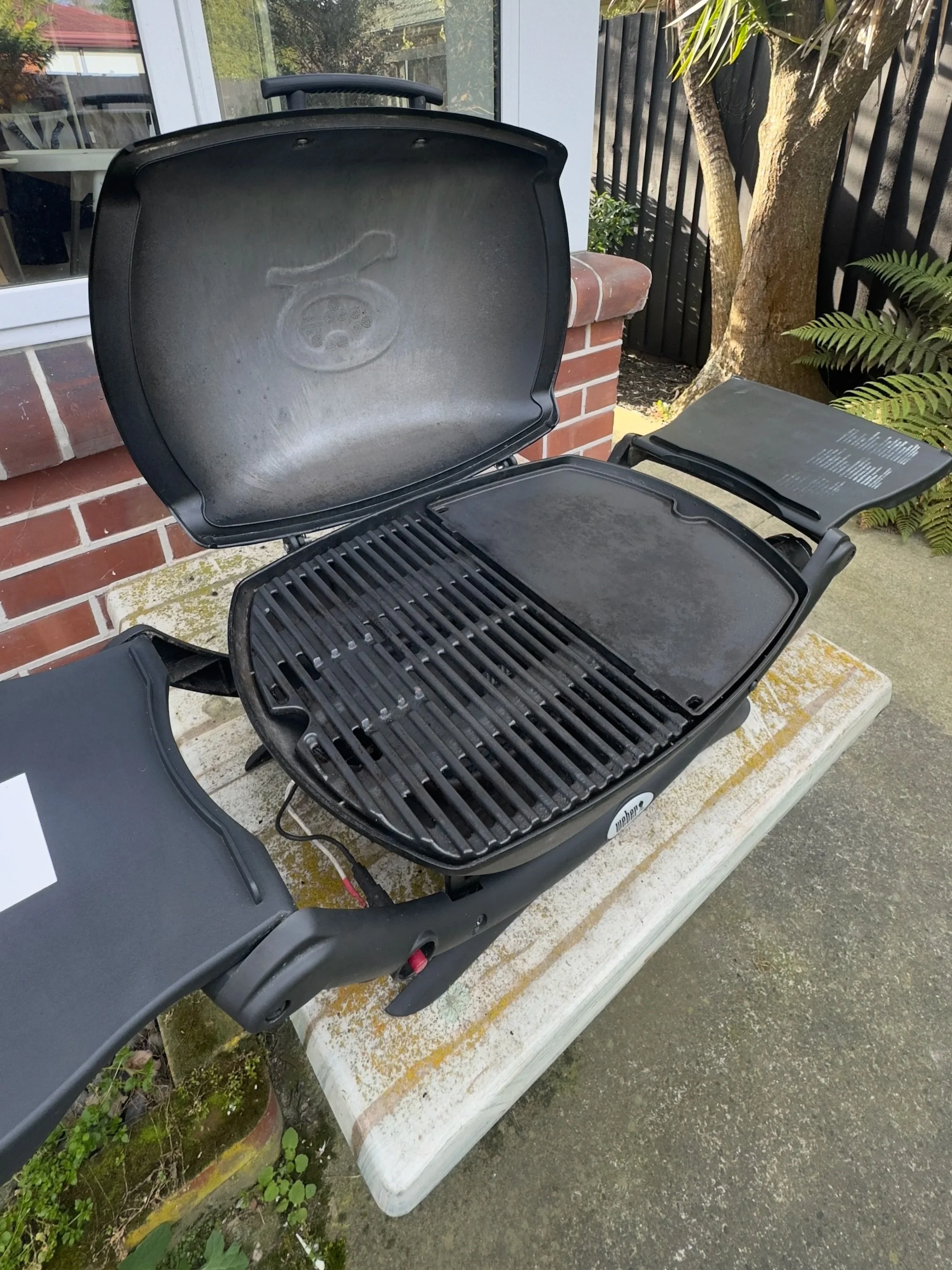 Open electric grill with a cooking surface and lid, placed on an outdoor table.