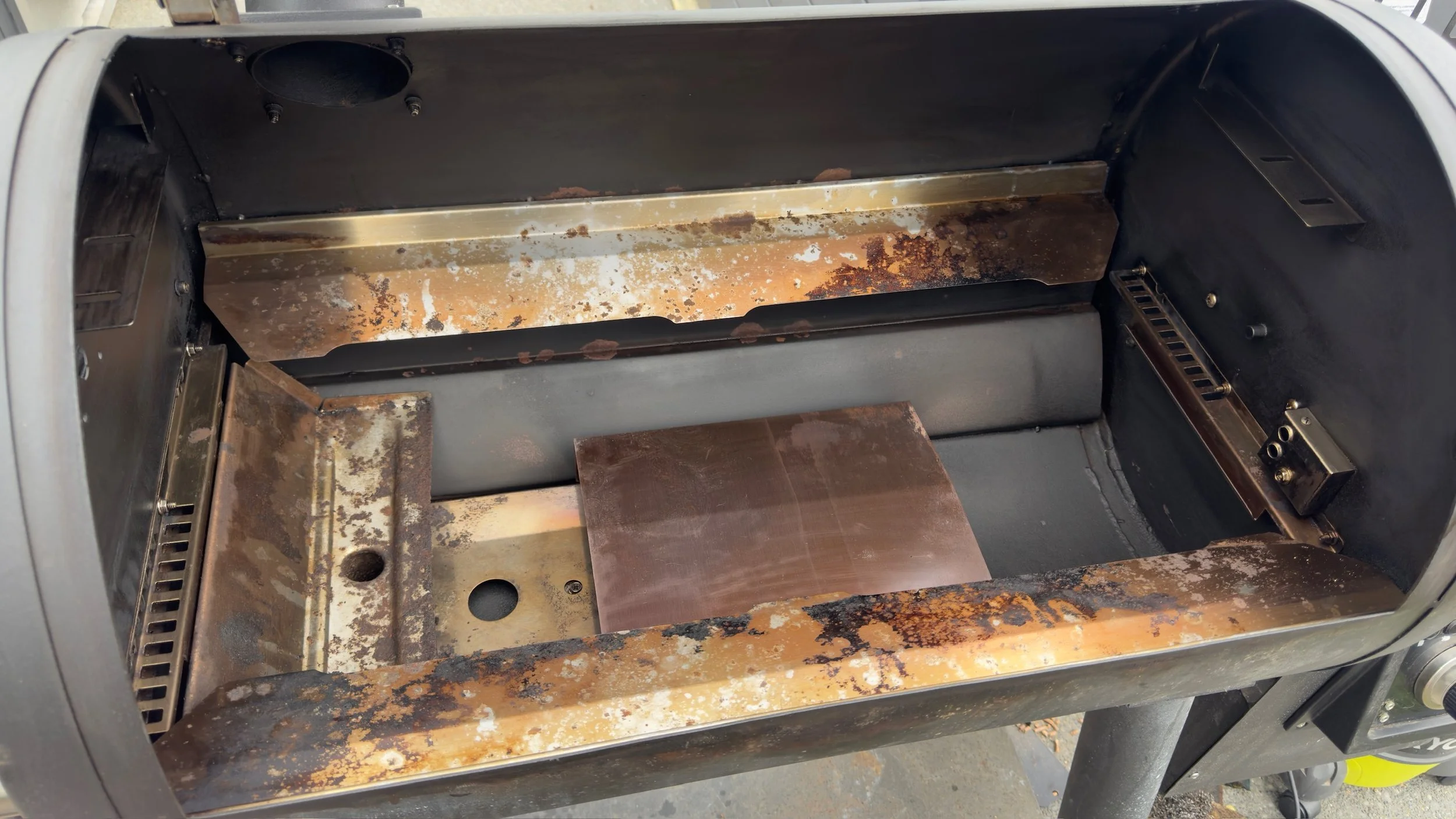 Inside view of a rusty, partially disassembled stainless steel oven or grill with corroded interior surfaces and exposed components.