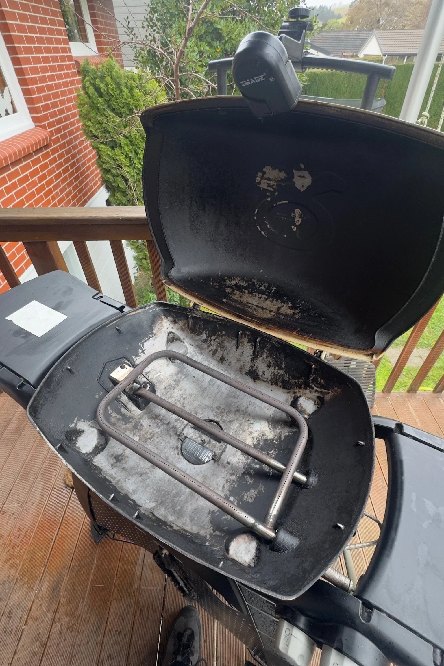Empty black charcoal grill with open lid, standing on a wooden deck outdoors, with some white ash remnants inside.