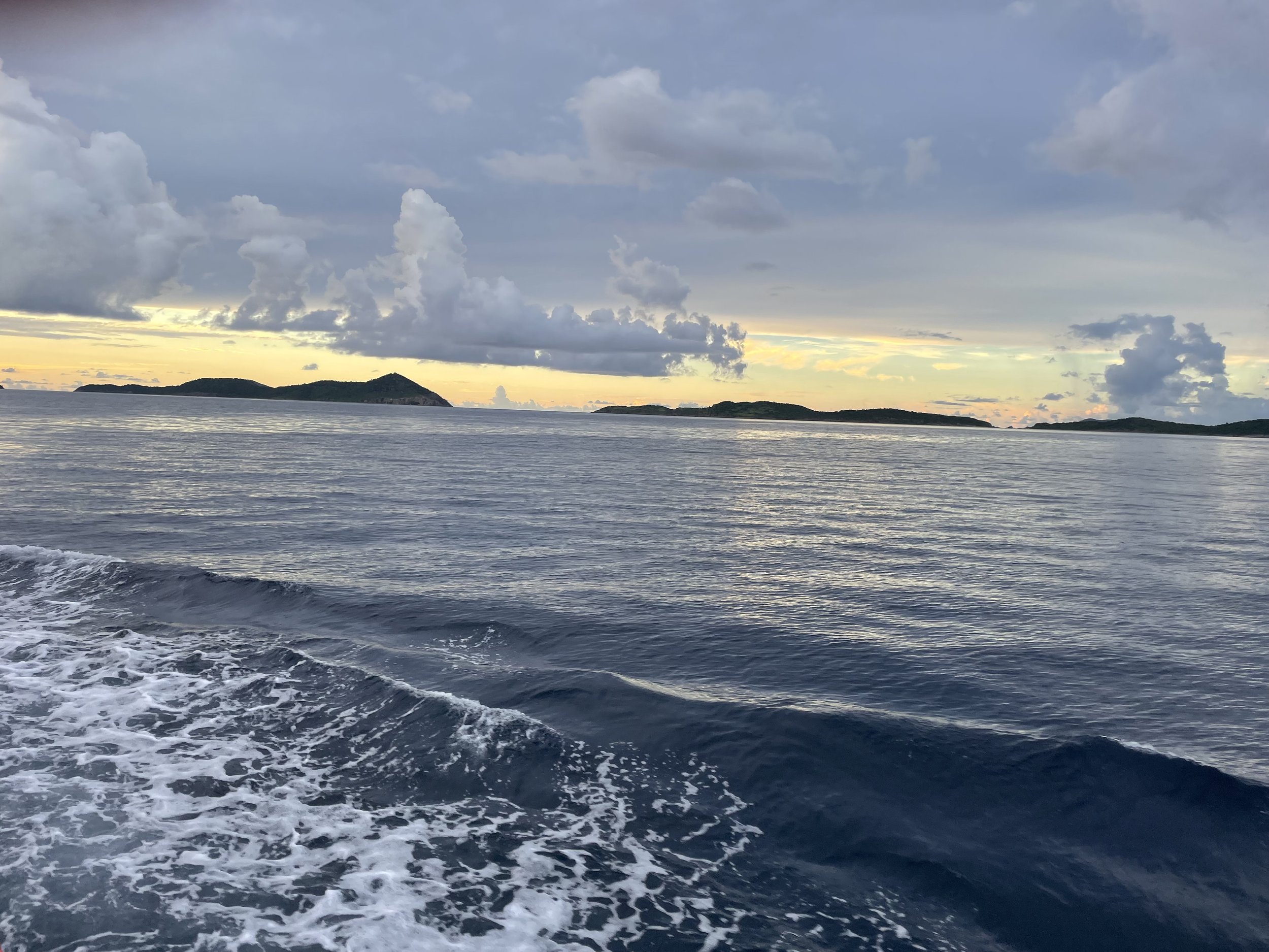 Ocean with small waves and distant islands under a partly cloudy sky at sunset or sunrise.