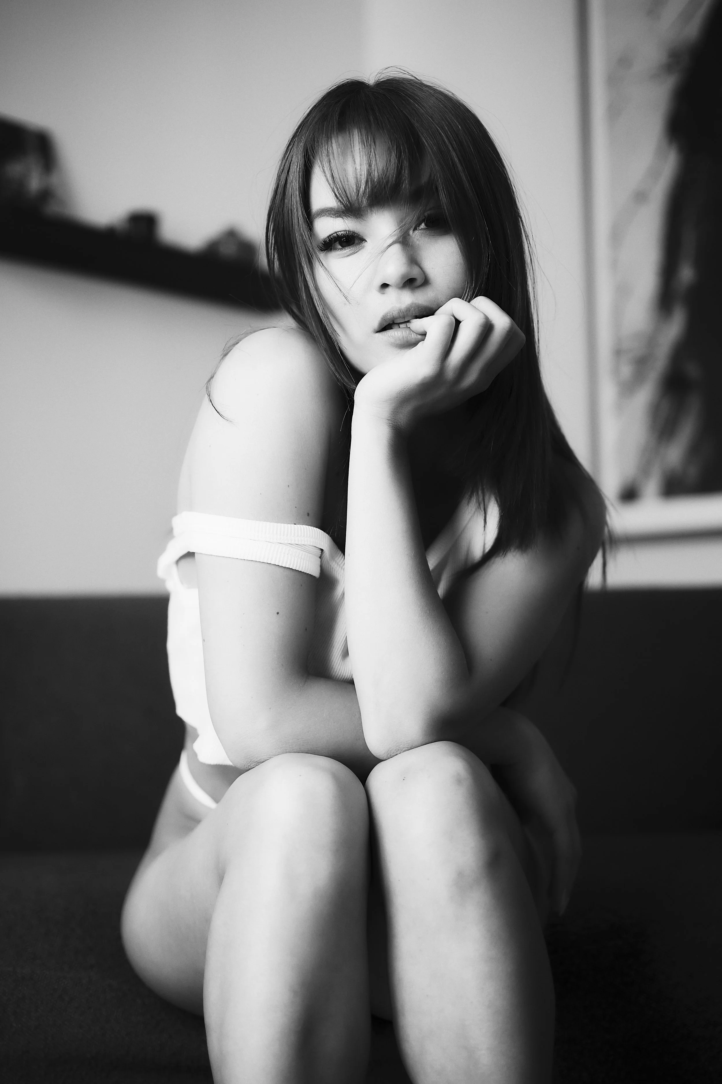 Photo en noir et blanc pour séance boudoir. Une jeune femme aux cheveux mi-longs et coiffés avec des franges, assise sur un canapé, regardant l'objectif avec une expression légèrement pensative.
