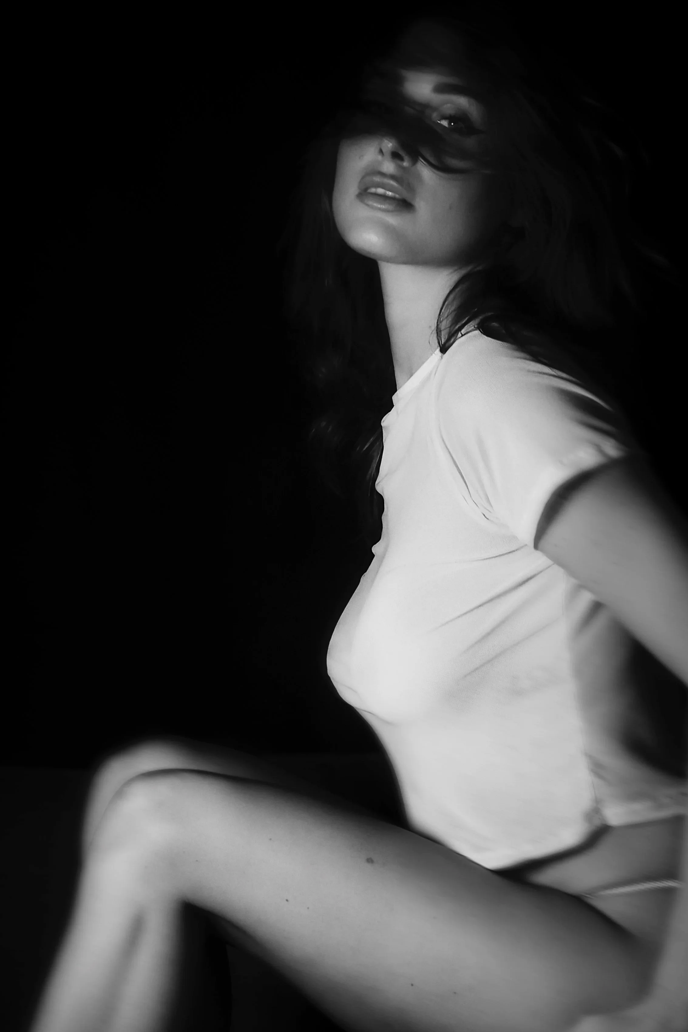 Photo pour séance portrait intimiste. Portrait en noir et blanc d'une femme avec cheveux mi-longs, portant un t-shirt blanc, regardant vers l'objectif, avec un fond noir.