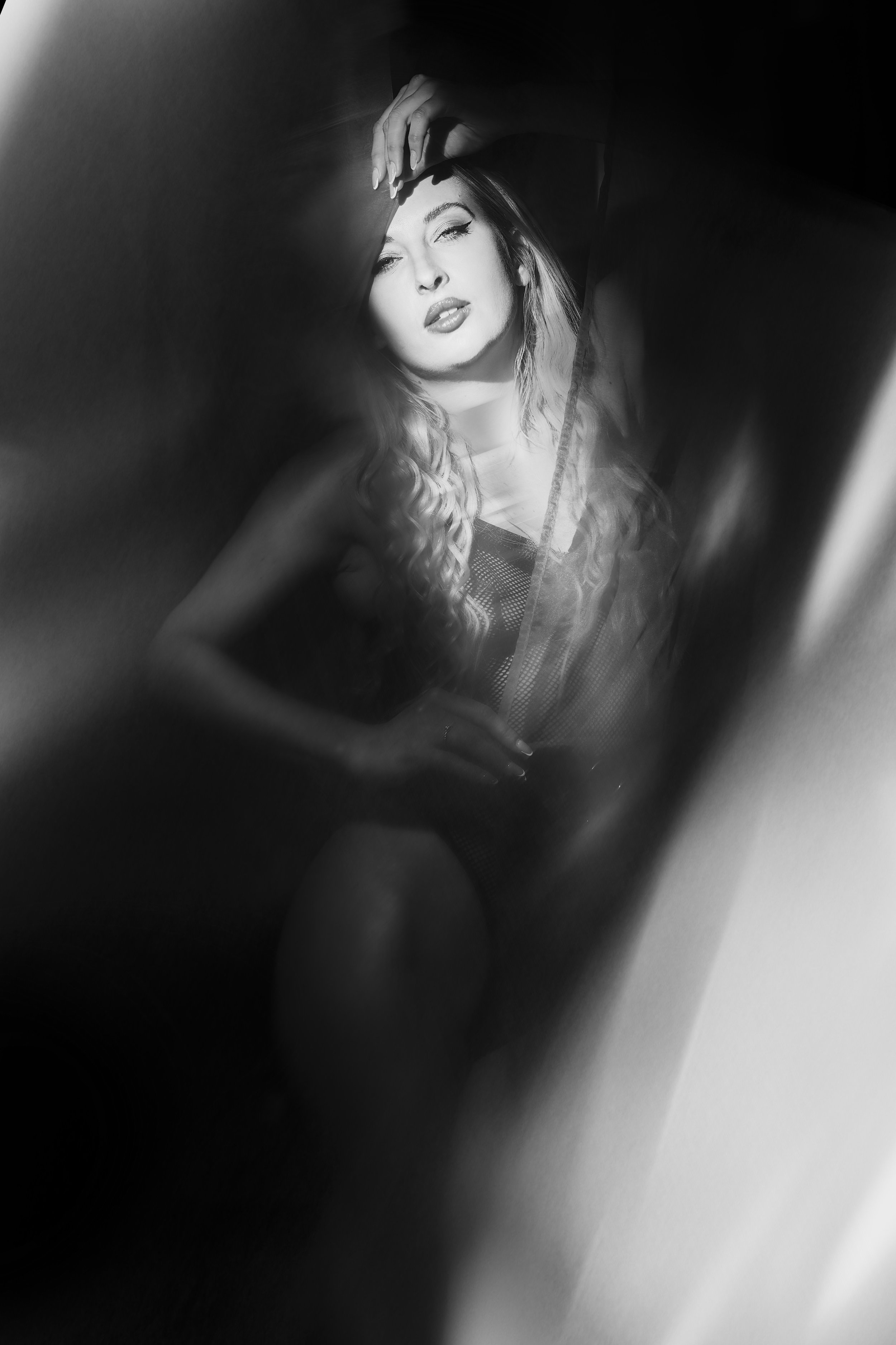 Séance portrait intimiste. Une femme posant, en noir et blanc, avec une expression séduisante et une pose élégante entourée d'un voile et jeux de lumière. Paris. Boudoir. Photographe intimiste. Intimate photographer.