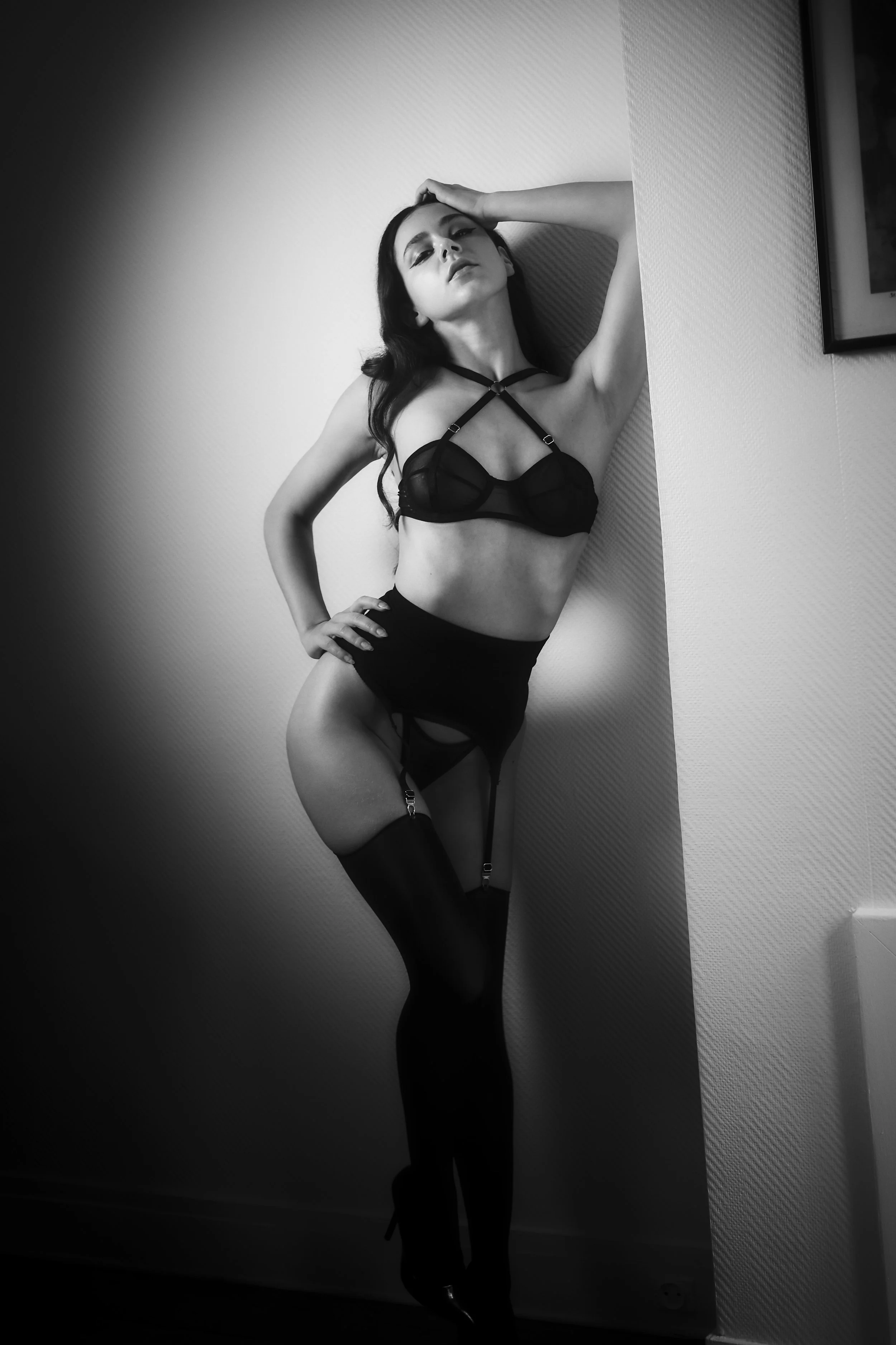 Photo pour séance boudoir. Femme posant contre un mur, portant des vêtements en lingerie noire, avec une expression confiante et une pose sophistiquée.