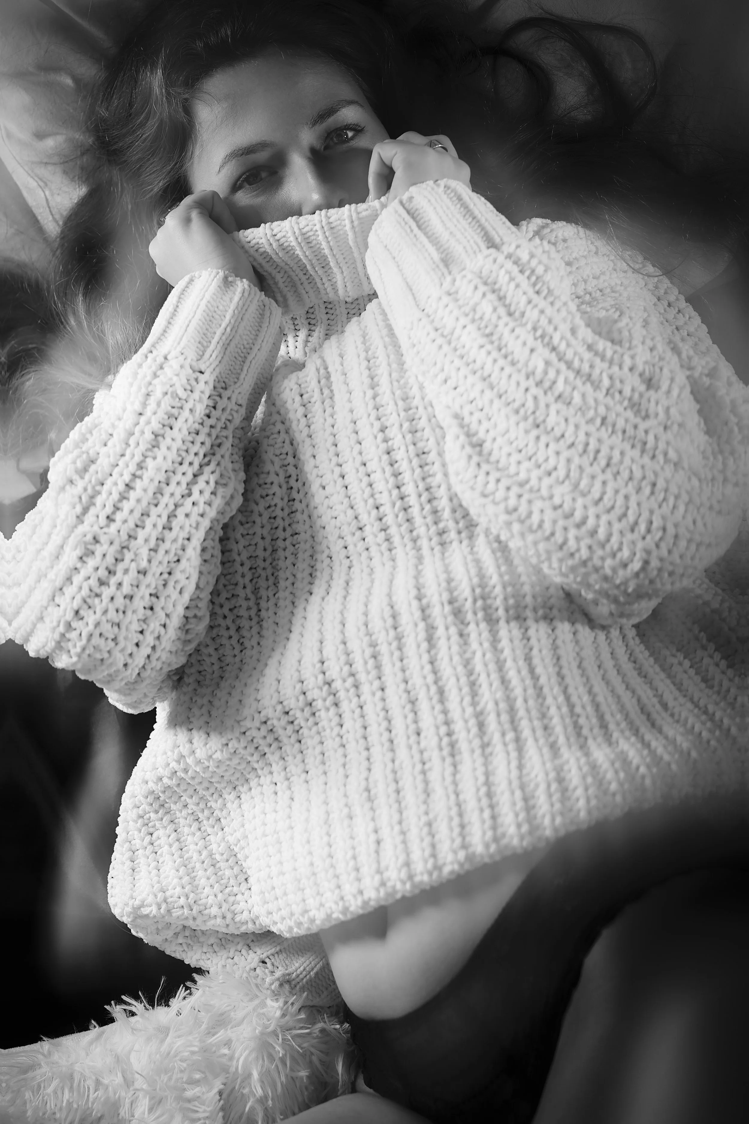 Photo pour séance Portrait Intimiste. Femme allongée, portant un pull en tricot, couvrant partiellement son visage, regardant la caméra.