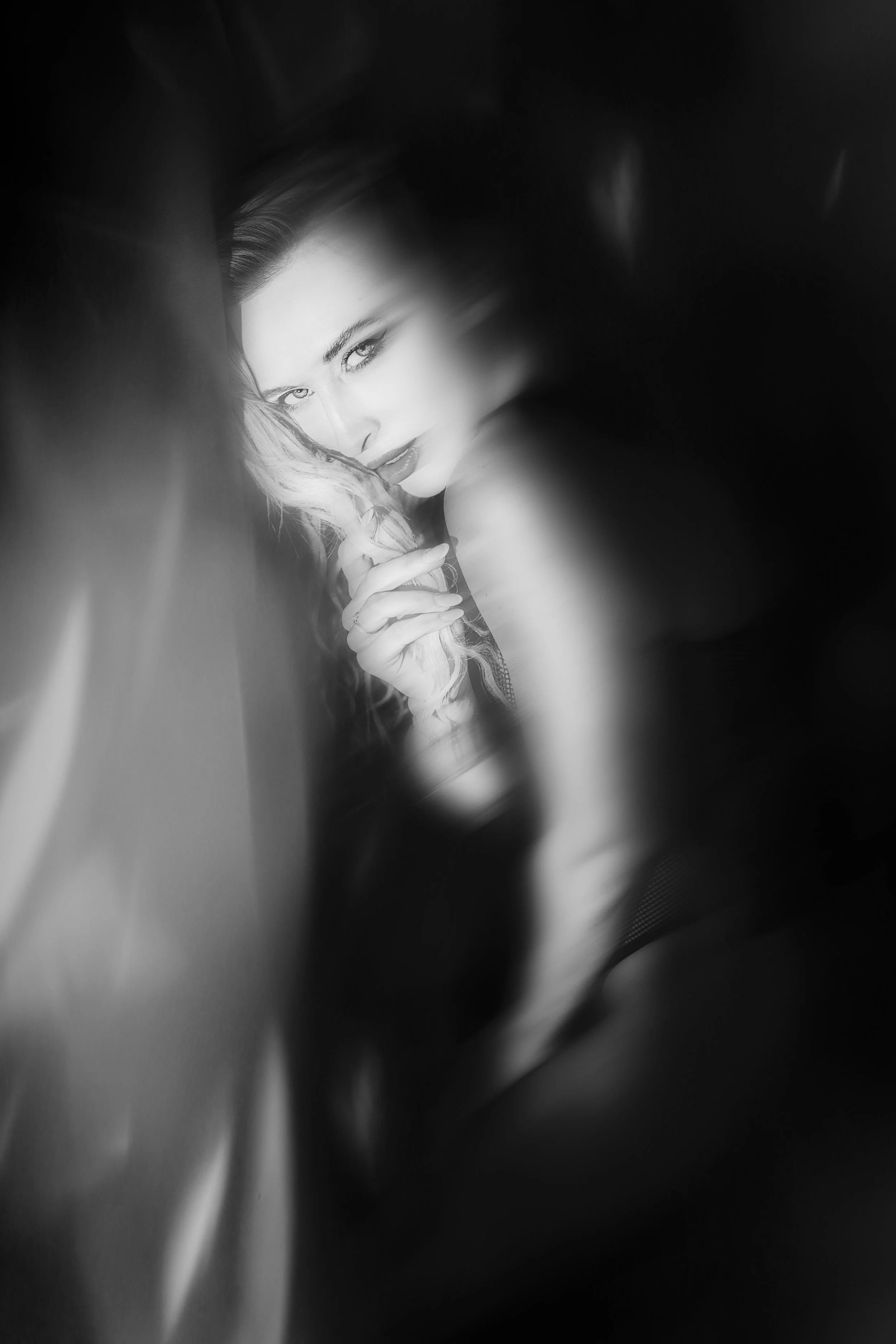 Une photo en noir et blanc d'une femme regardant l'objectif, avec un éclairage doux et flou autour du visage