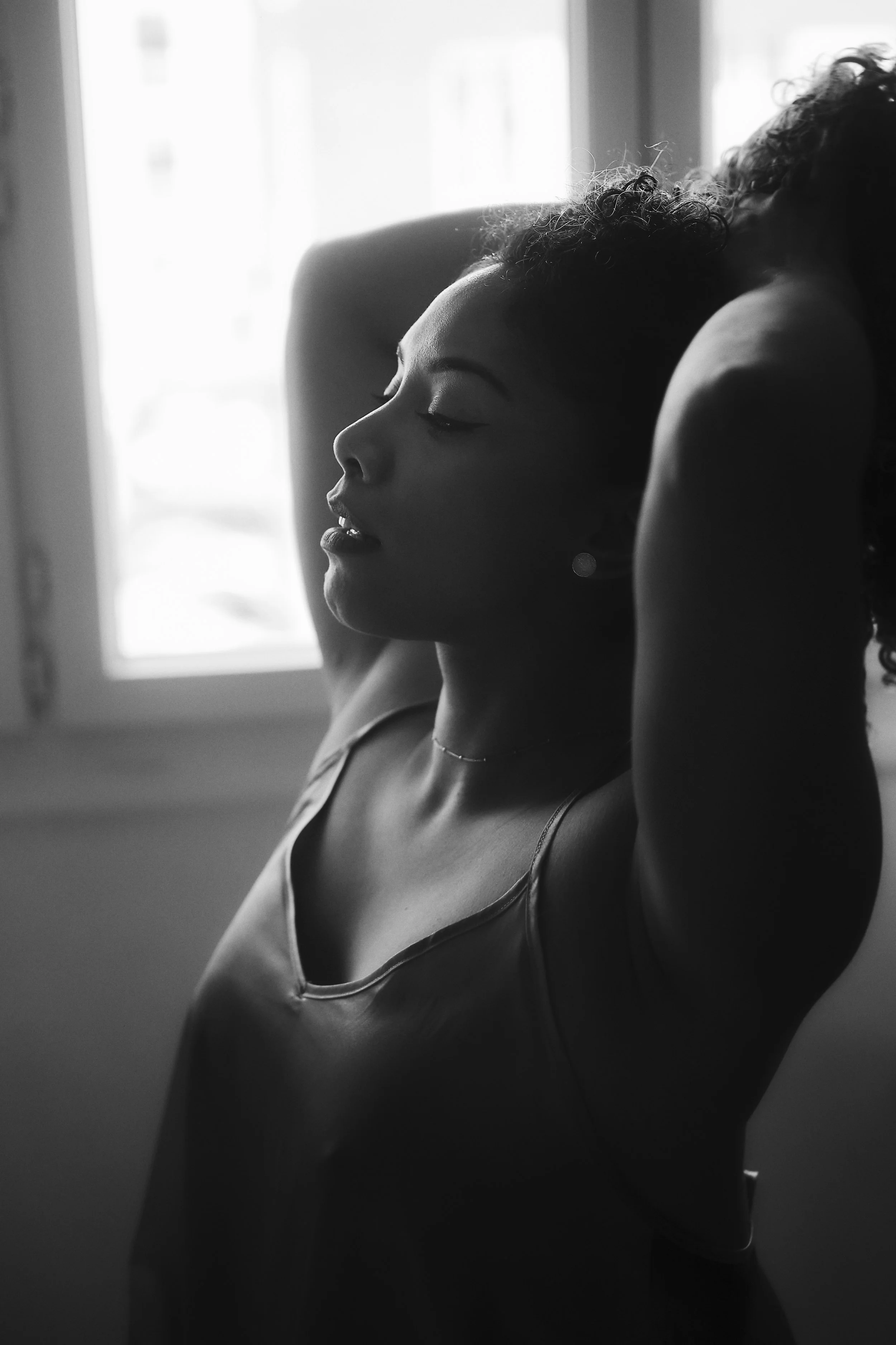 Photo pour séance portrait intimiste. Une femme aux cheveux courts, de profil, avec les yeux fermés, en lingerie, posant près d'une fenêtre. Image en noir et blanc.