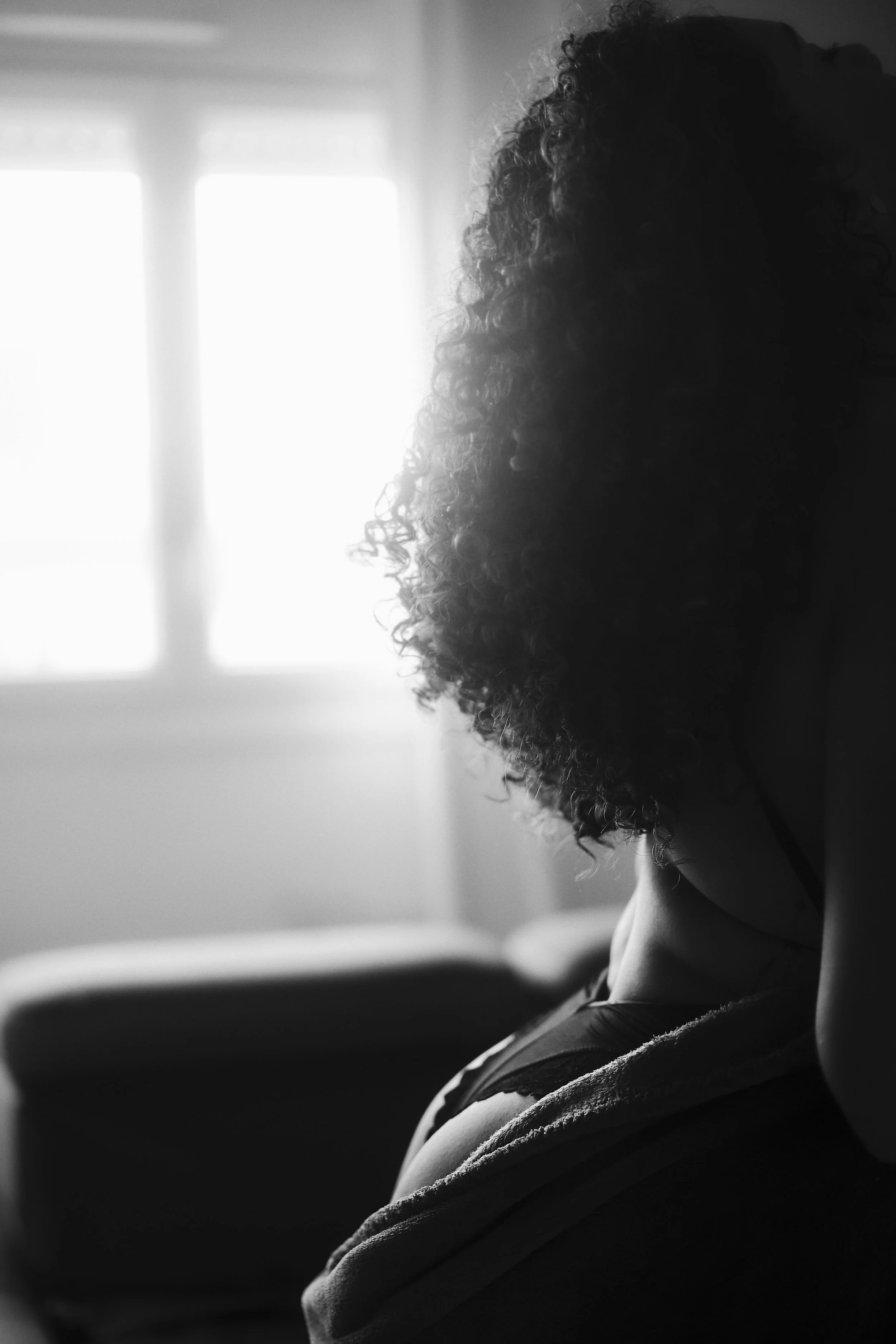 Photo pour séance charme. Profil d'une personne à cheveux bouclés assise dans la lumière naturelle d'une fenêtre