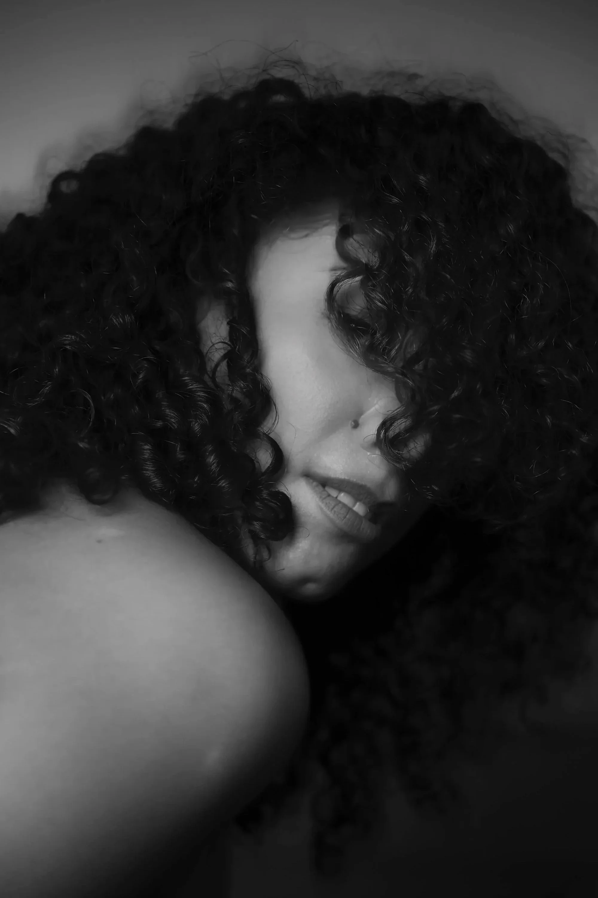 Un gros plan en noir et blanc d'une femme avec de longs cheveux bouclés, souriante légèrement, en position inclinée.