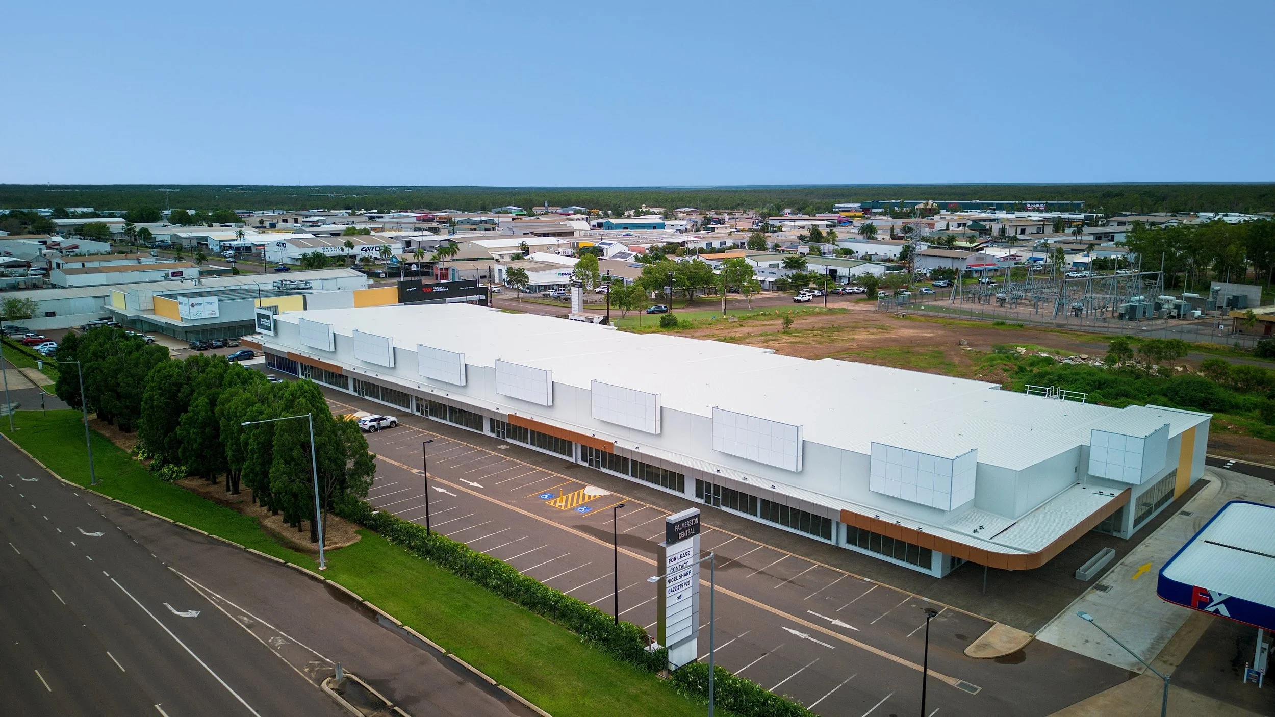 A modern building with large windows, a curved gold-colored band, and square architectural features; surrounded by a parking lot with cars and people walking nearby.