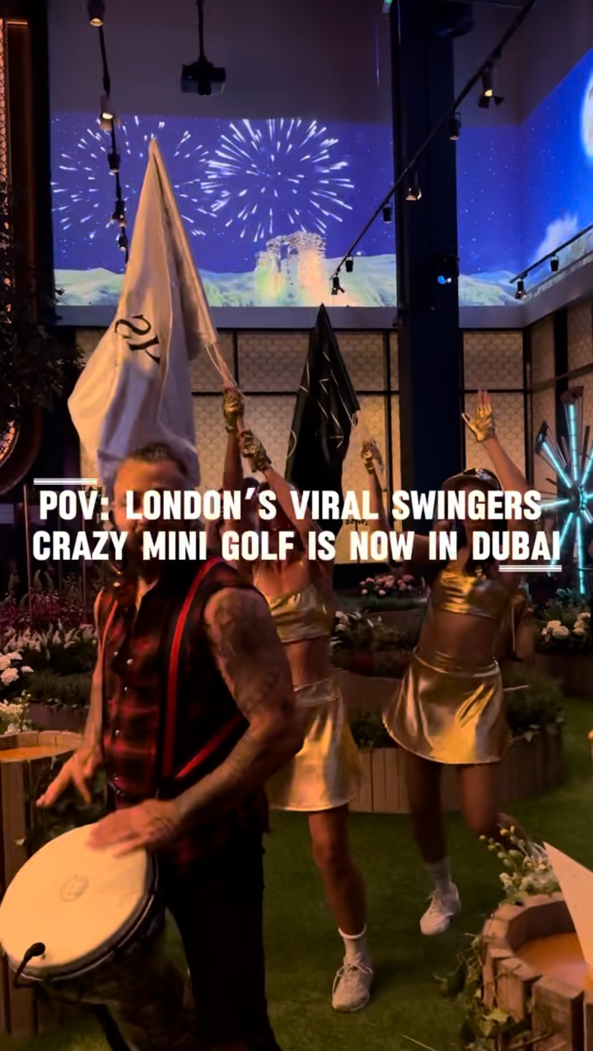 People celebrating with flags and a drummer inside a venue with fireworks and full moon projection on a screen