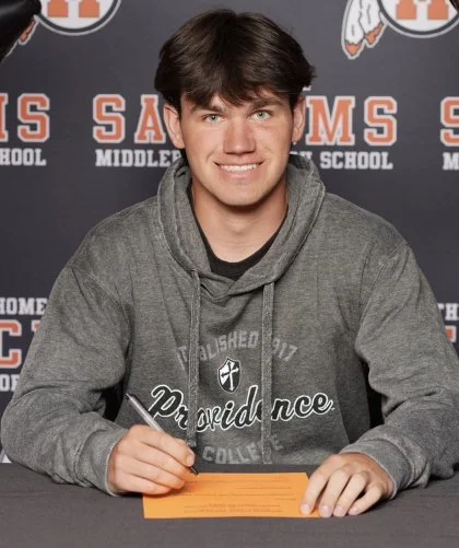 Young man signing a document at a table with a school backdrop