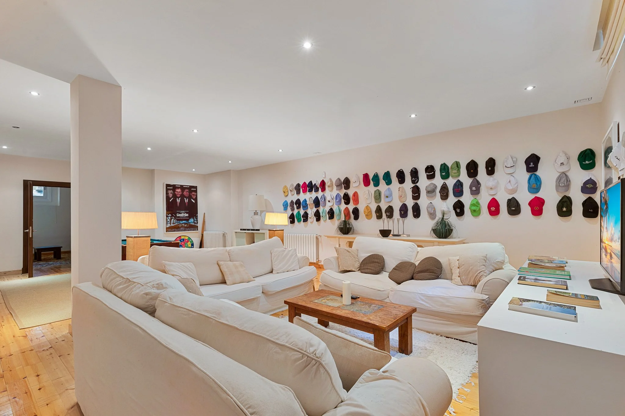 Living room with beige couches, a wooden coffee table, and a wall decorated with many colorful hats.