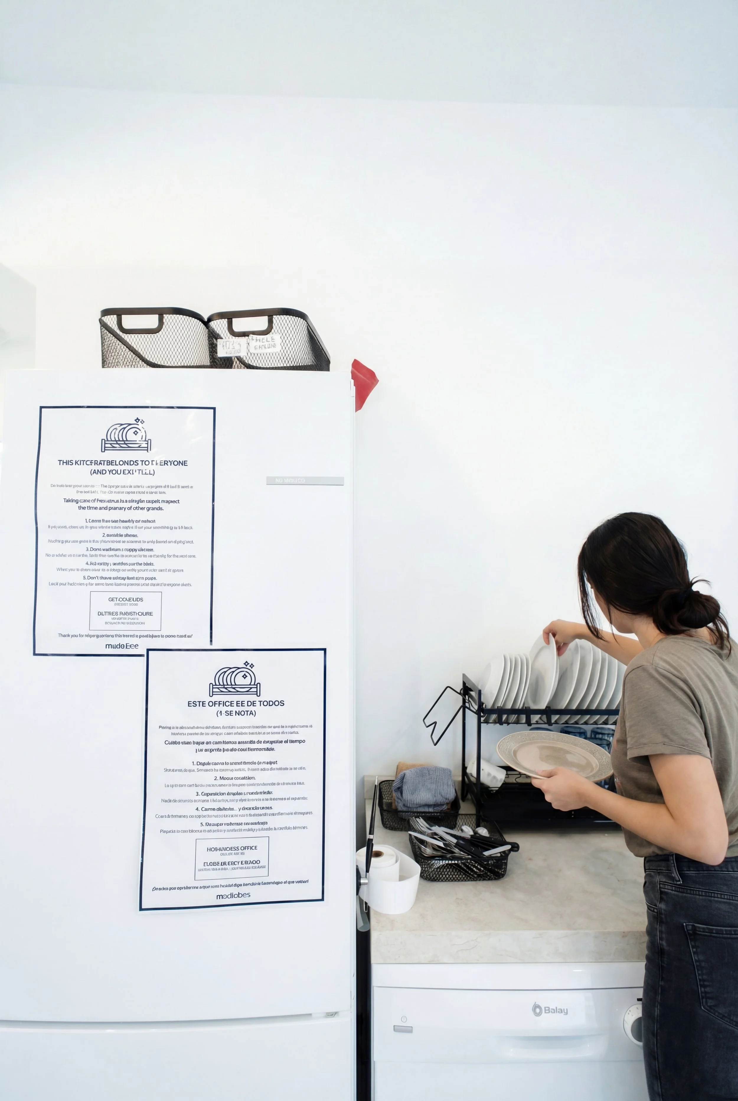 Huésped colocando platos en el escurridor junto a la nevera y el lavavajillas en la zona común del hostel.