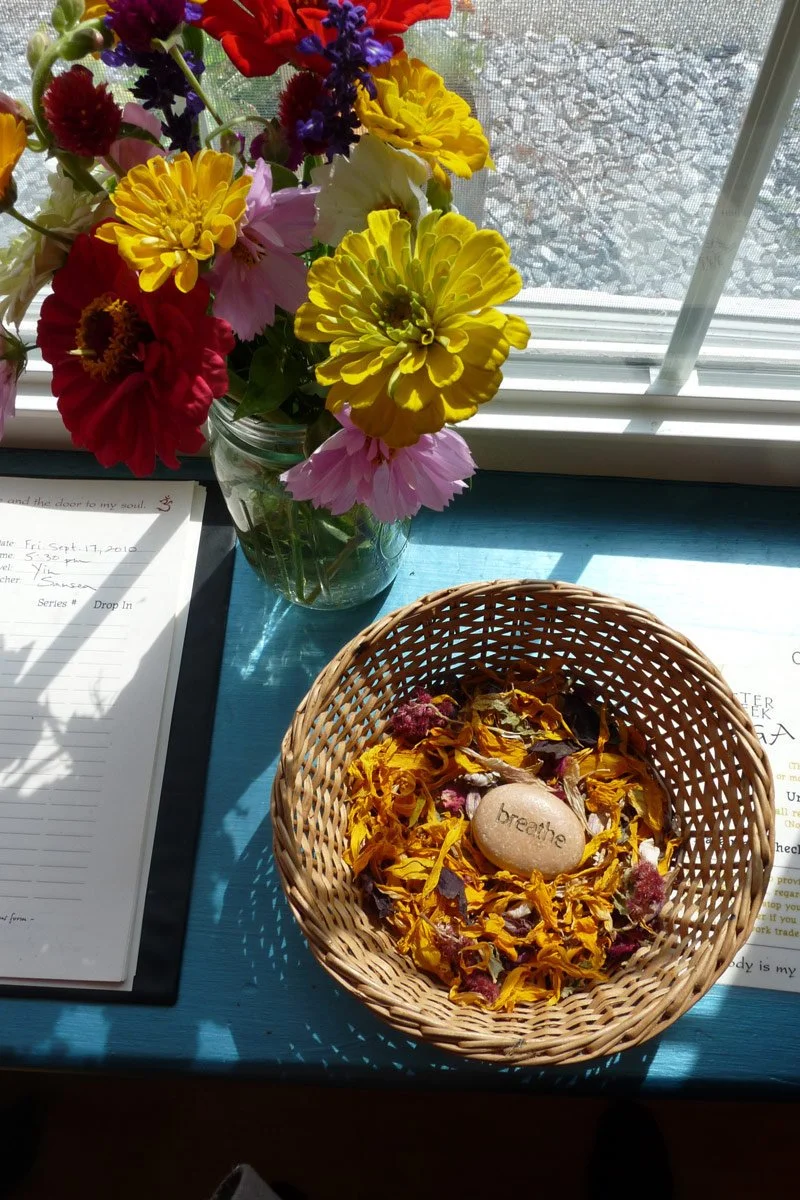 A basket of flower petals and small rock engraved with the work "Breathe"
