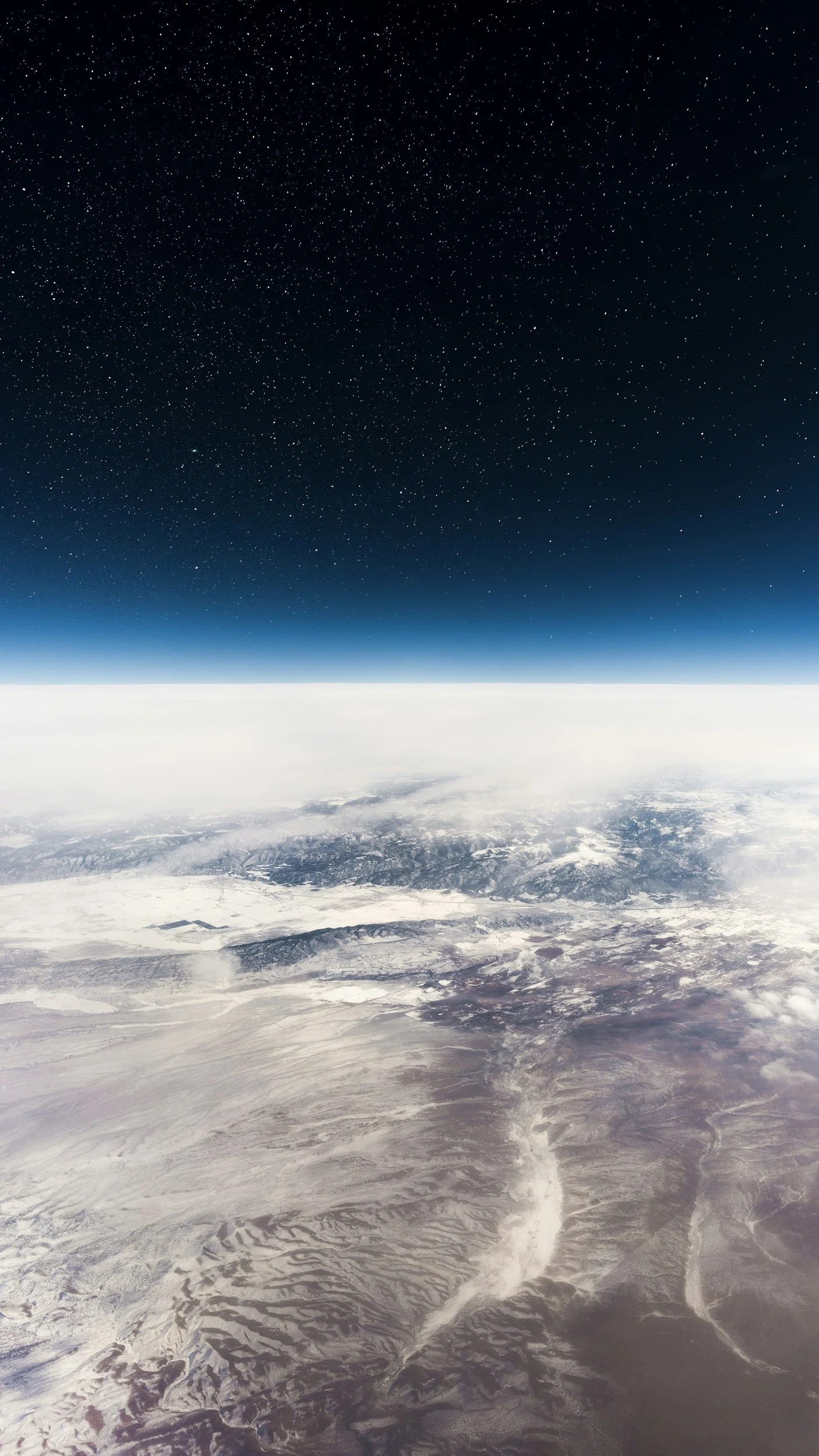 Vues de la Terre depuis l'espace montrant un ciel étoilé et un paysage terrestre enneigé avec des montagnes et des formations désertiques.
