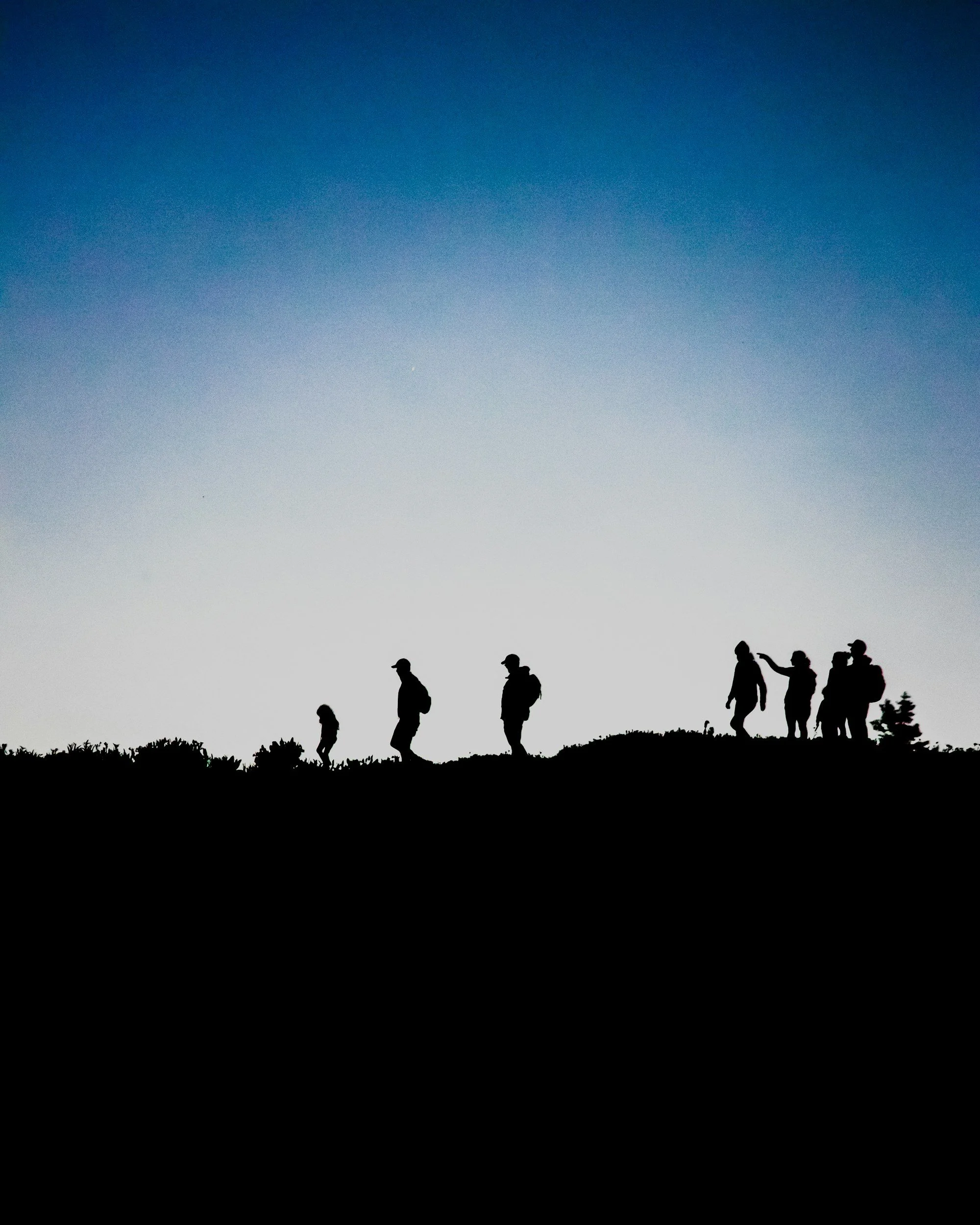 Silhouettes de personnes faisant une randonnée en montagne lors du coucher ou du lever du soleil.