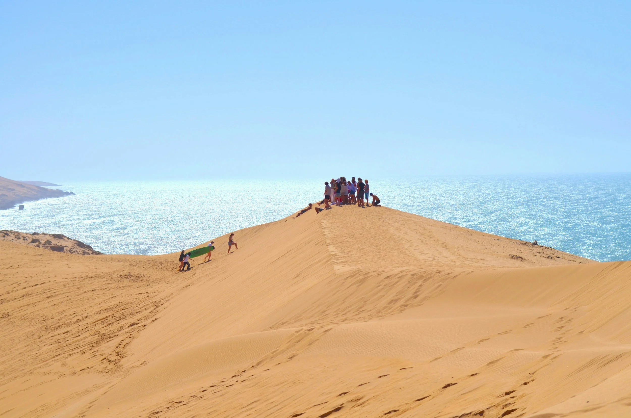 Groupe de personnes sur une dune de sable avec vue sur la mer en arrière-plan, ciel clair.