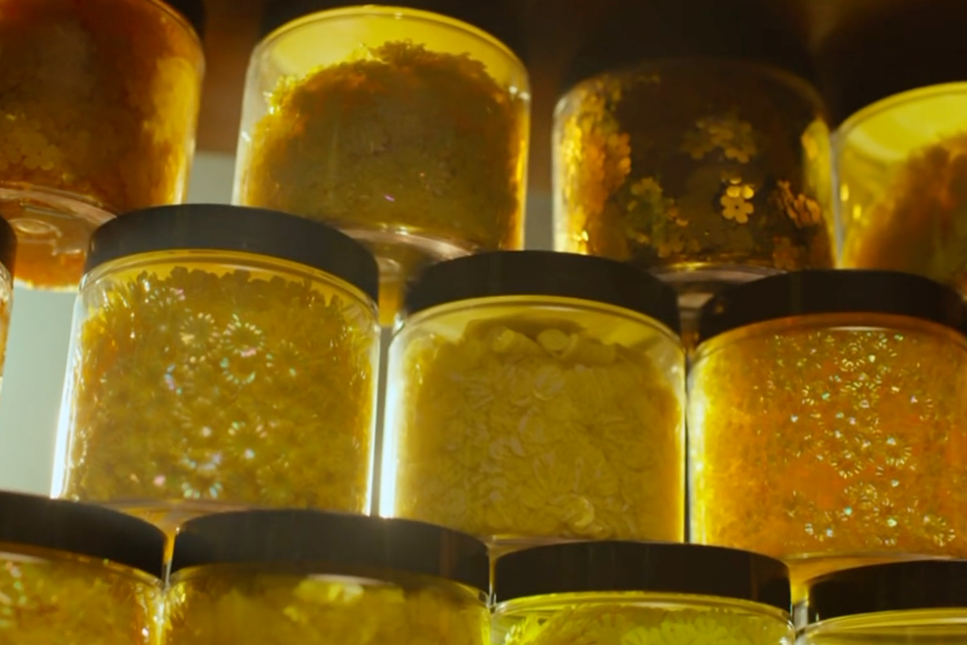 Close-up of several glass jars filled with beads and sequins, stacked on top of each other, with black lids.