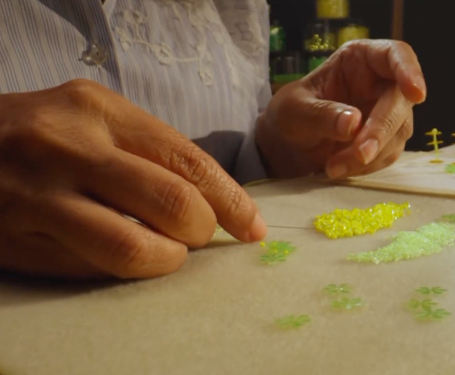 Close-up of Artist's hands working with  yellow and green beads or sequins on a beige surface.