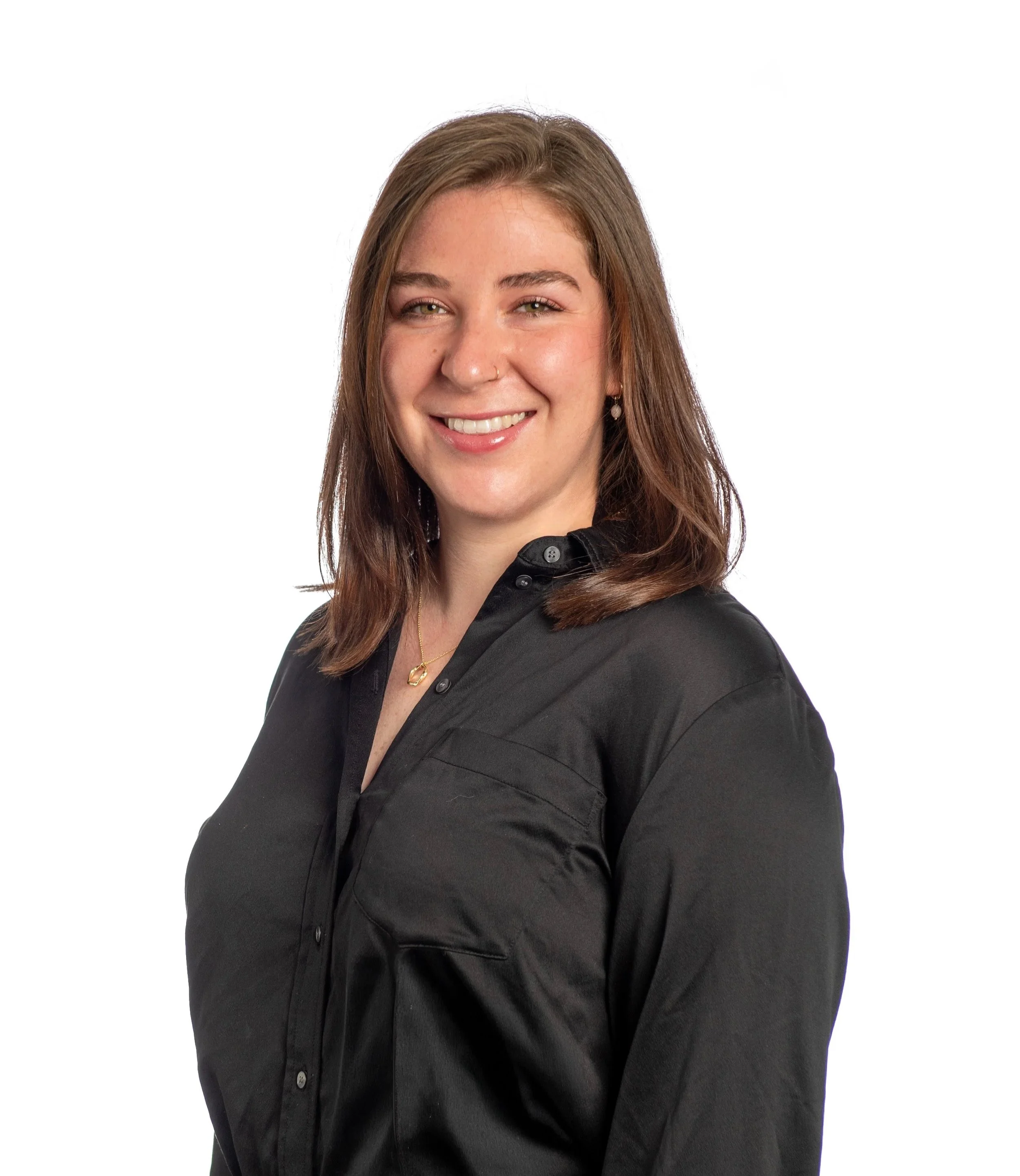A young woman with shoulder-length brown hair and fair skin smiling, wearing a black dress shirt standing against a white background.