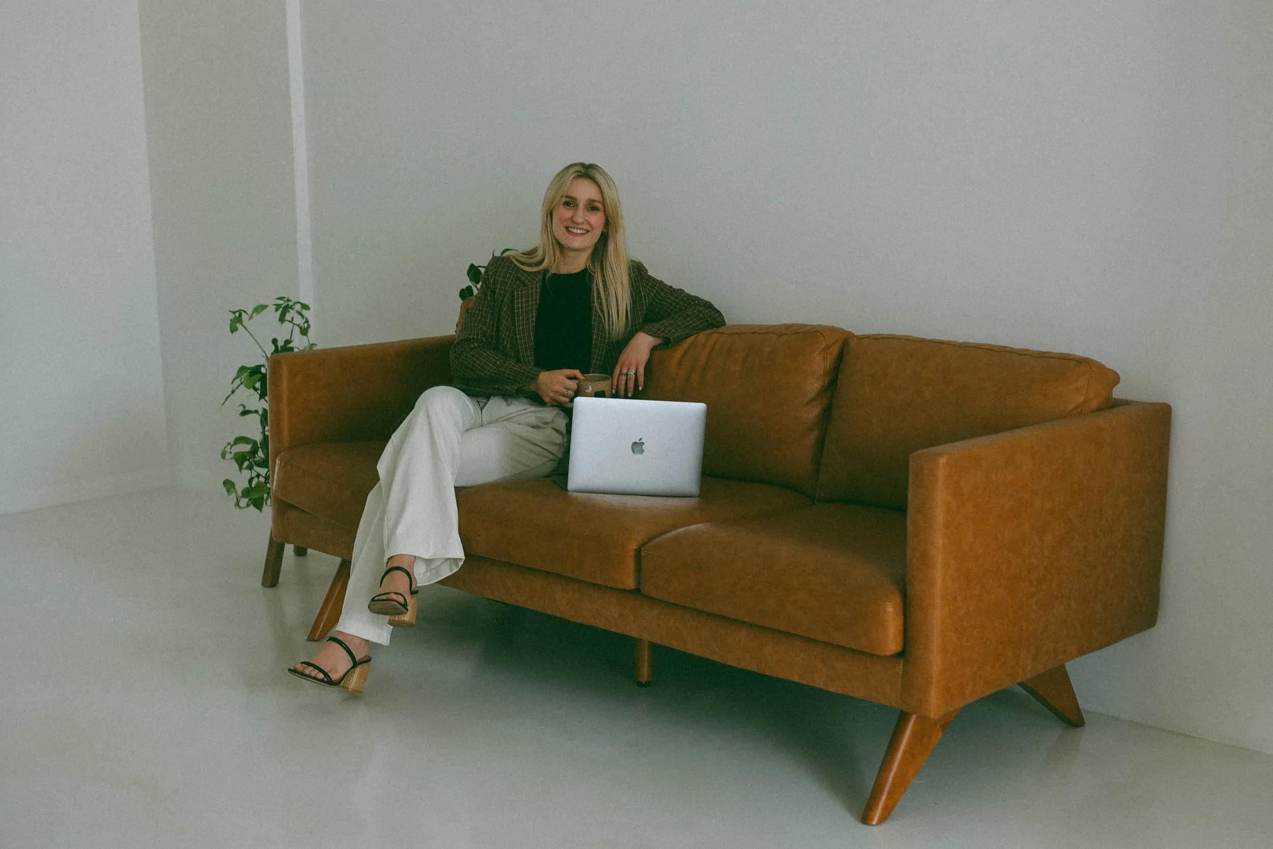 Brooke Terry, LPC  Blonde hair trauma professional sitting on a leather couch with coffee in hand. Specializes in treating anxiety,  grief, and trauma.