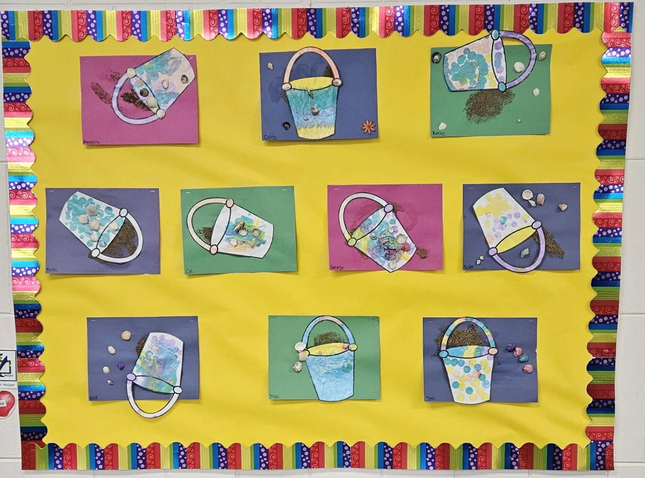 Classroom bulletin board with colorful decorated paper buckets and mixed materials, featuring student names, on yellow background bordered by rainbow-colored strips.