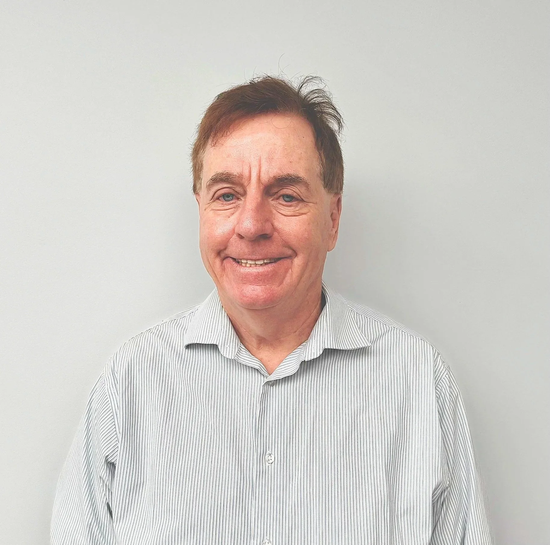 Photograph of a person wearing a striped button-up shirt standing against a plain light-colored wall. The person's face is obscured.