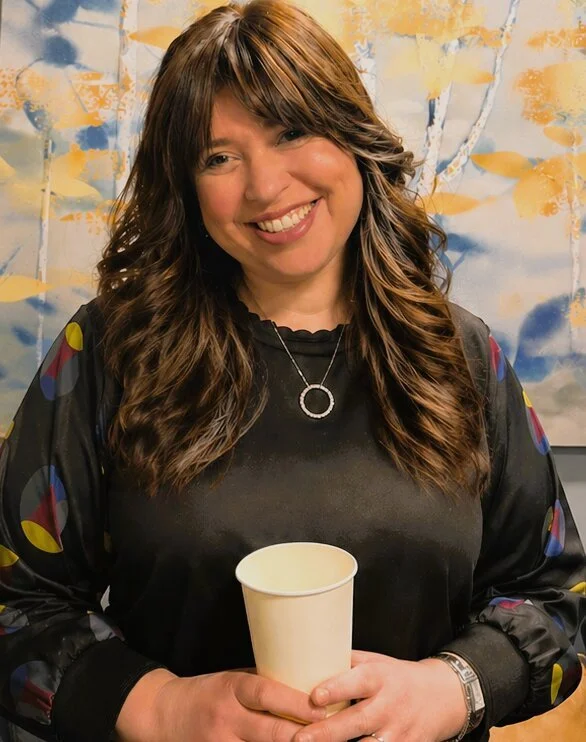young woman with brown hair holding coffee cup and smiling