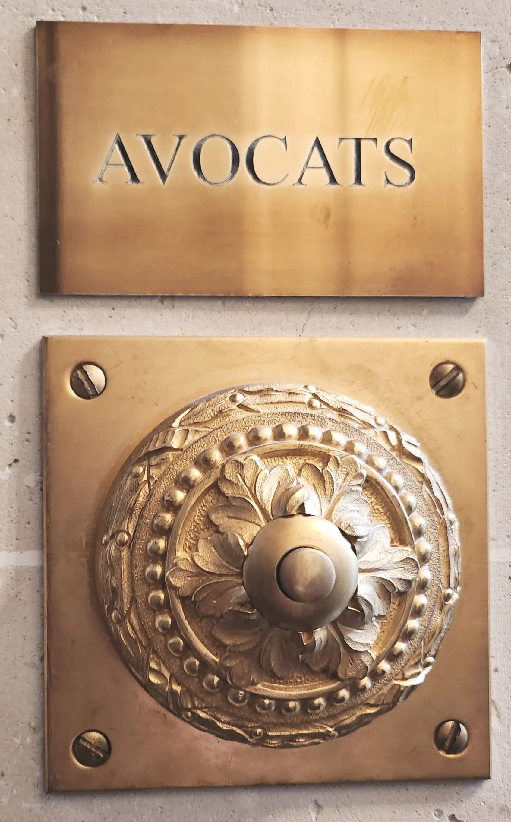 Plaque rectangulaire en métal avec l'inscription 'AVOCATS' et un bouton de porte doré ornée de détails floraux.