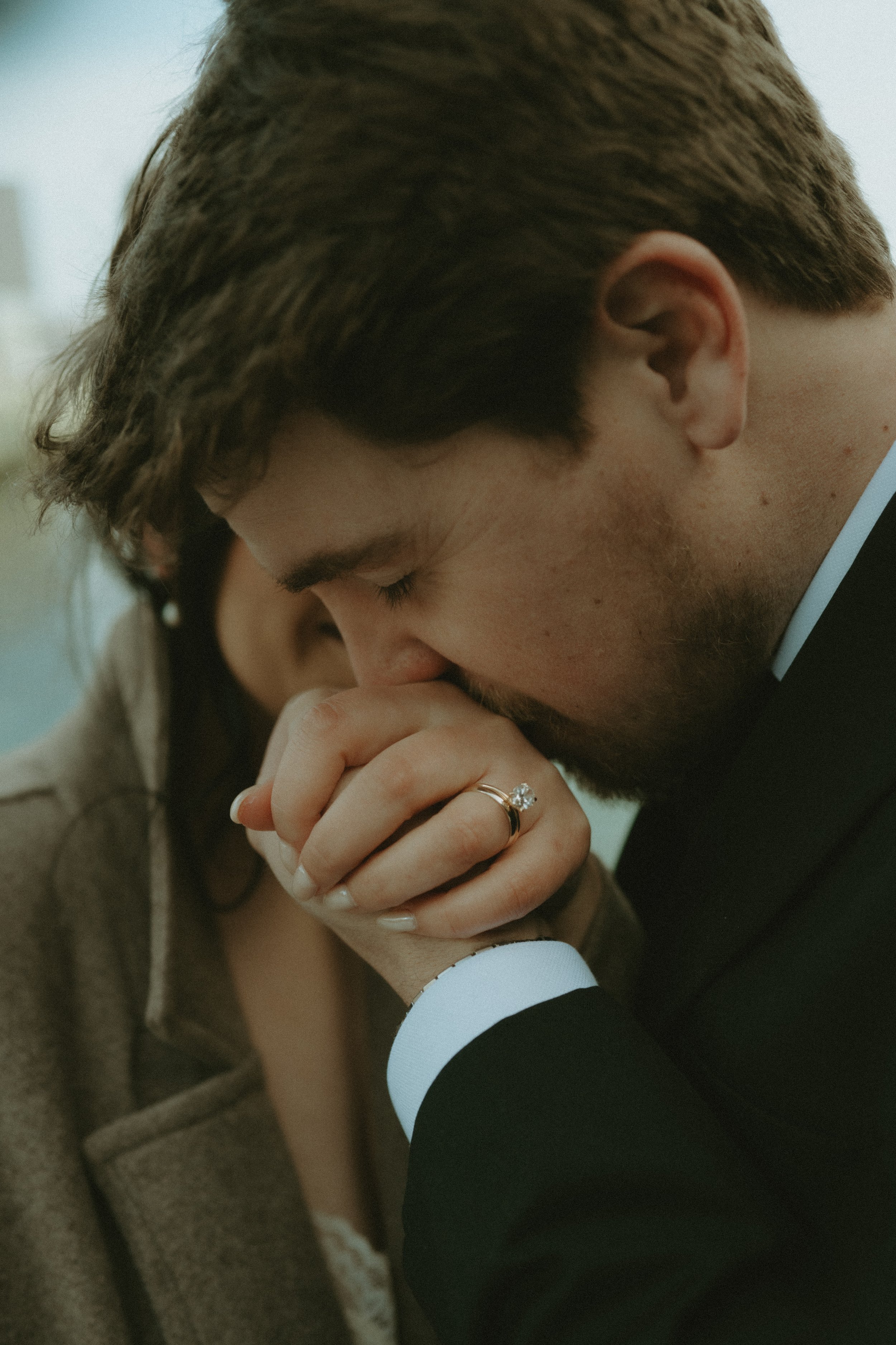 A man in a suit kissing a woman's hand, showing an engagement ring on her finger.