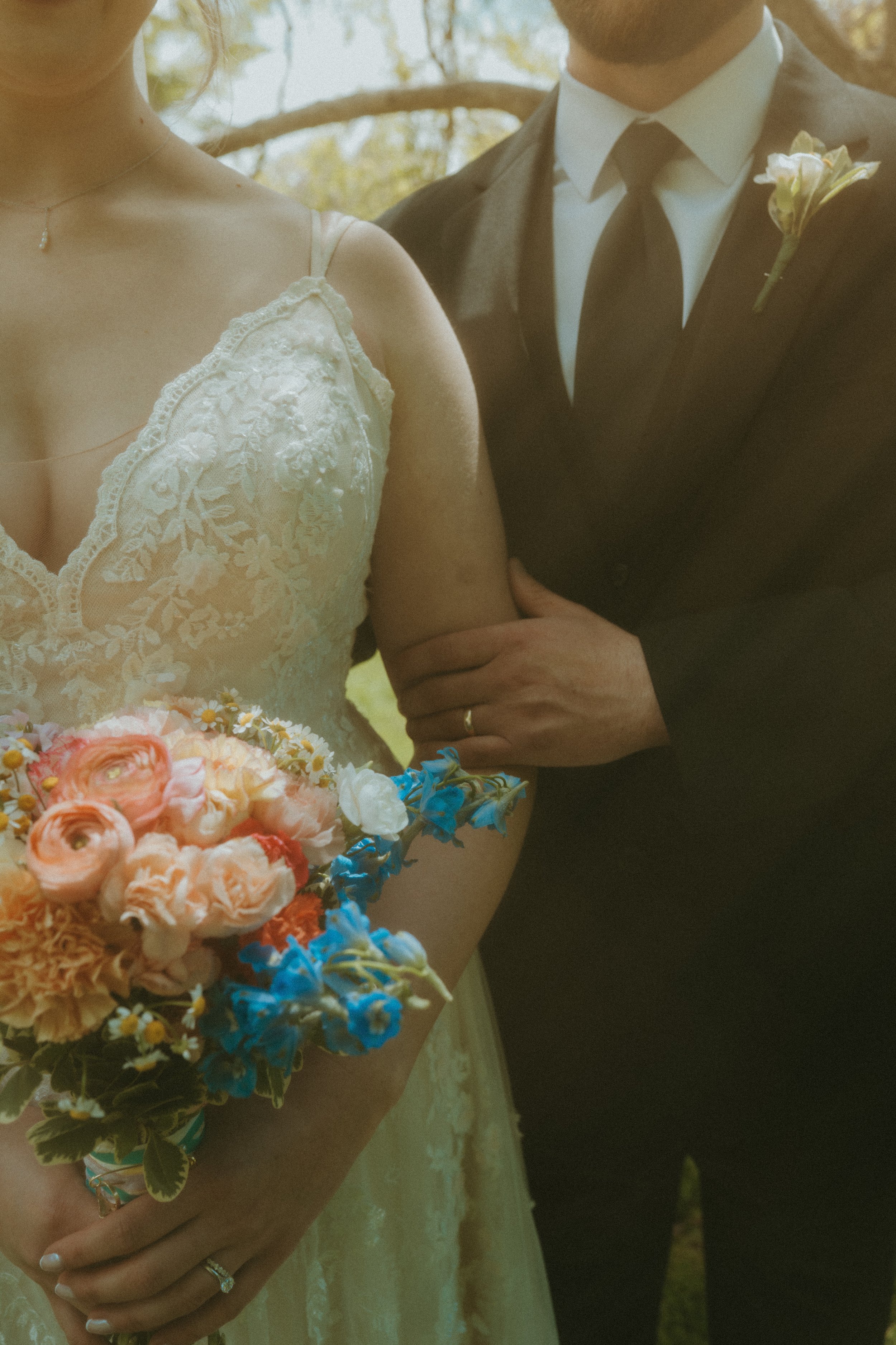 Close-up of bride and groom at wedding, bride holding a bouquet of pink, white, and blue flowers, groom wearing a dark suit with a boutonniere