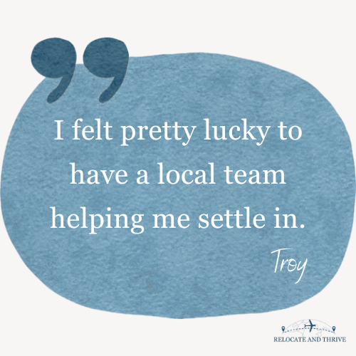 Scenic landscape of a large lake surrounded by green hills and tall mountains under a cloudy sky.