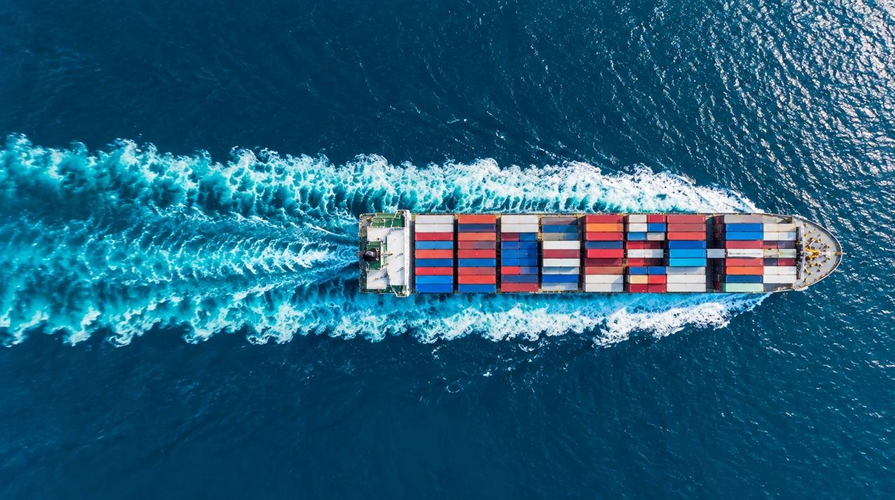 Aerial view of a container ship carrying colorful cargo containers through deep blue ocean water.