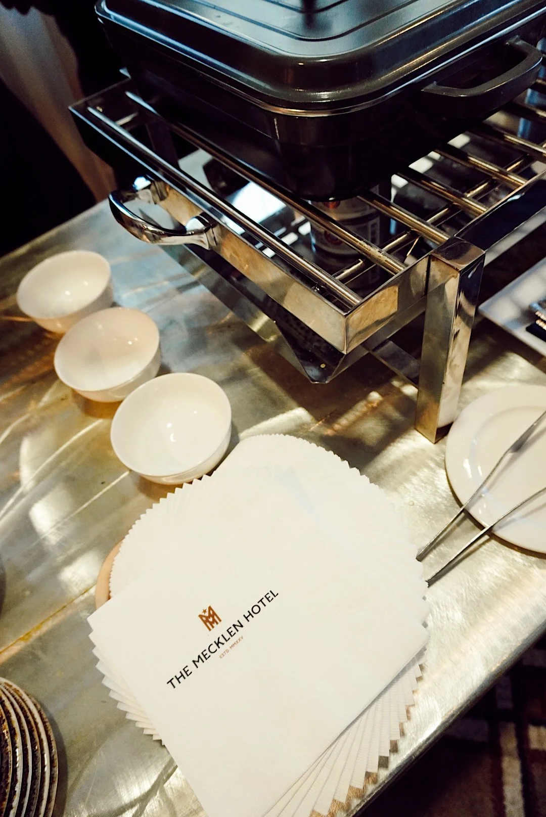 Stack of branded The Mecklen Hotel napkins placed beside serving dishes and catering equipment at an event food station.