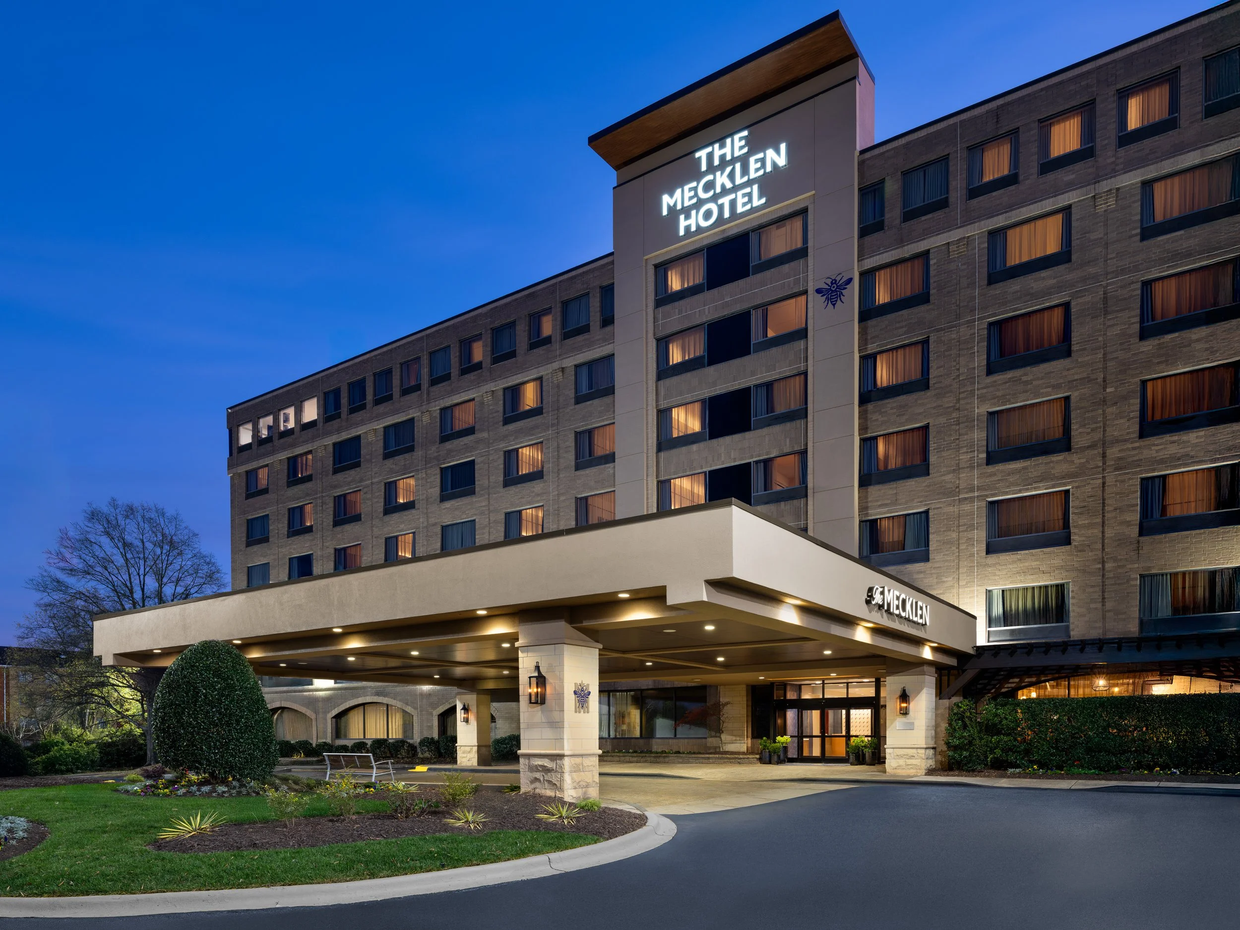 Exterior view of The Mecklen Hotel in Charlotte, North Carolina at dusk, with illuminated hotel signage above the entrance canopy.