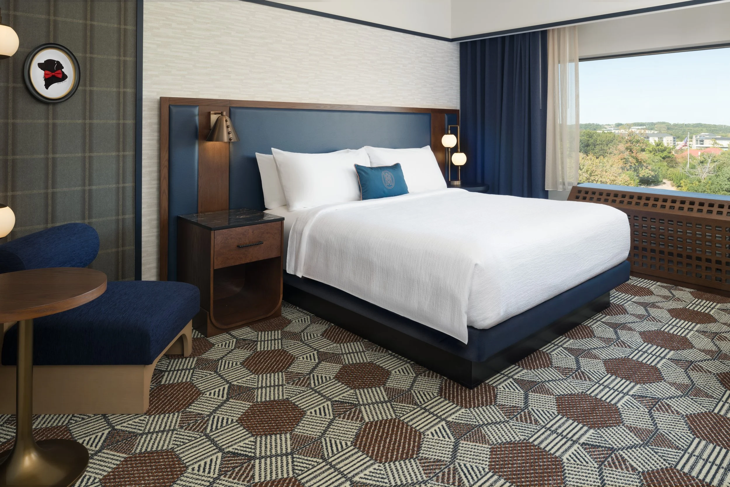 King guest room at The Mecklen Hotel in Charlotte featuring a plush king bed, modern lighting, seating area, patterned flooring, and large window with city views.