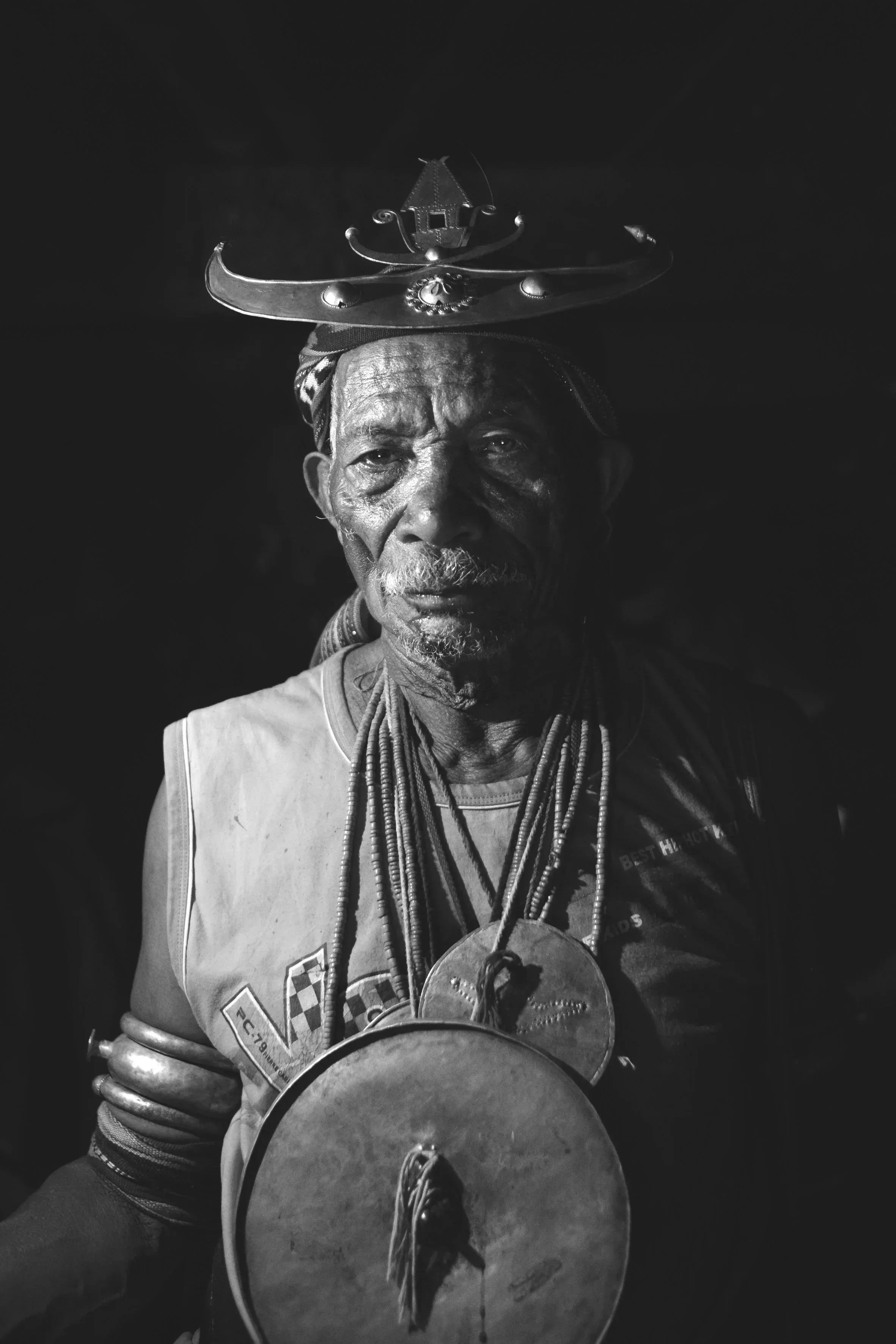 A portrait of an elderly man wearing traditional jewelry and a large headpiece from East Timor.