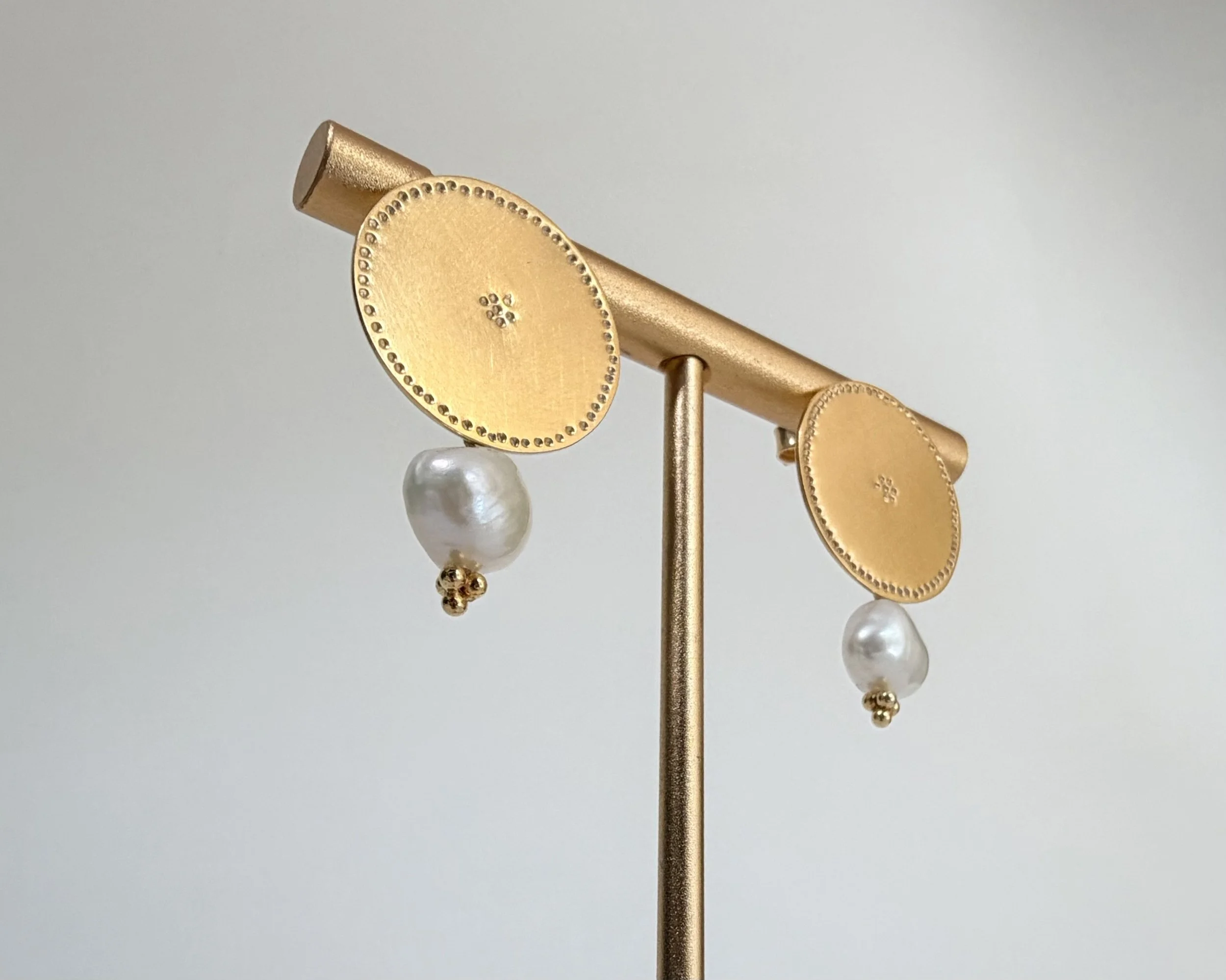 Angled view of the one-of-a-kind Pearl Belak earrings with hand-finished gold vermeil discs and freshwater pearls.