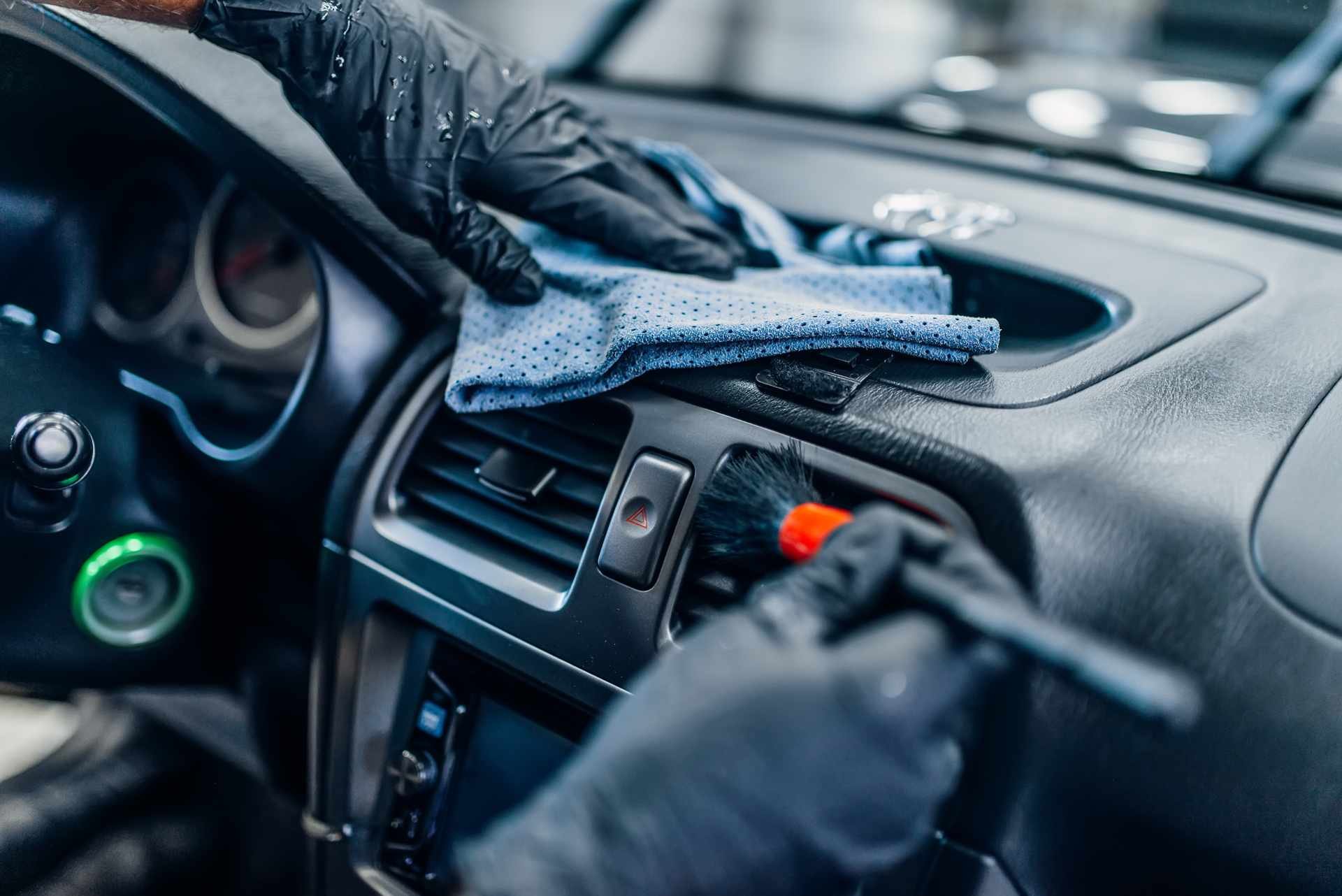 Personnes nettoyant l'intérieur d'une voiture avec des gants, un chiffon et une brosse, nettoyage du tableau de bord.