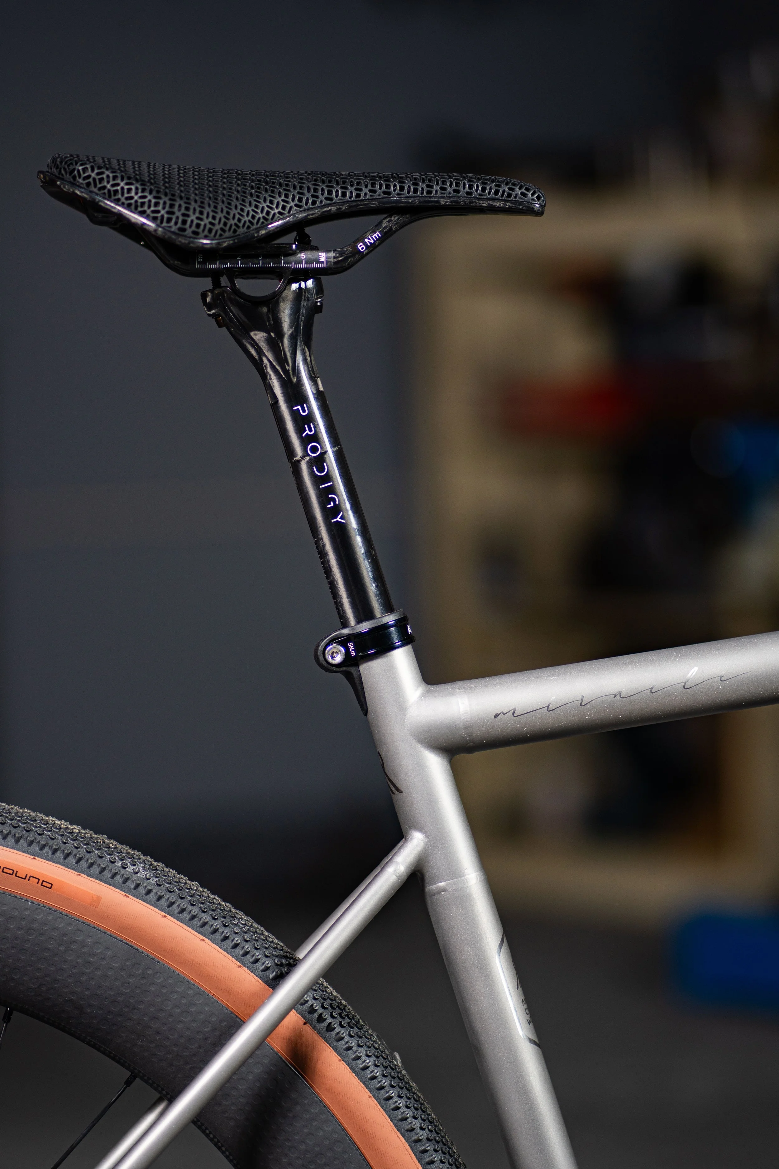 Close-up of a bicycle's saddle, seat post, and rear wheel with a black tire and orange sidewall.