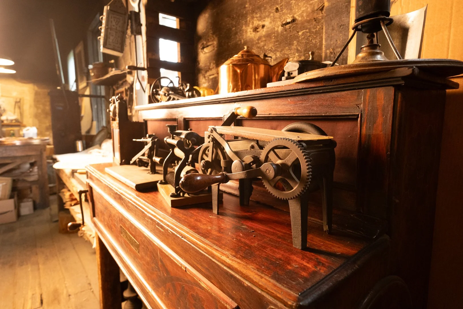 Vintage woodworking machines on a wooden table in a rustic workshop with wooden floors and walls, illuminated by natural light from a window.